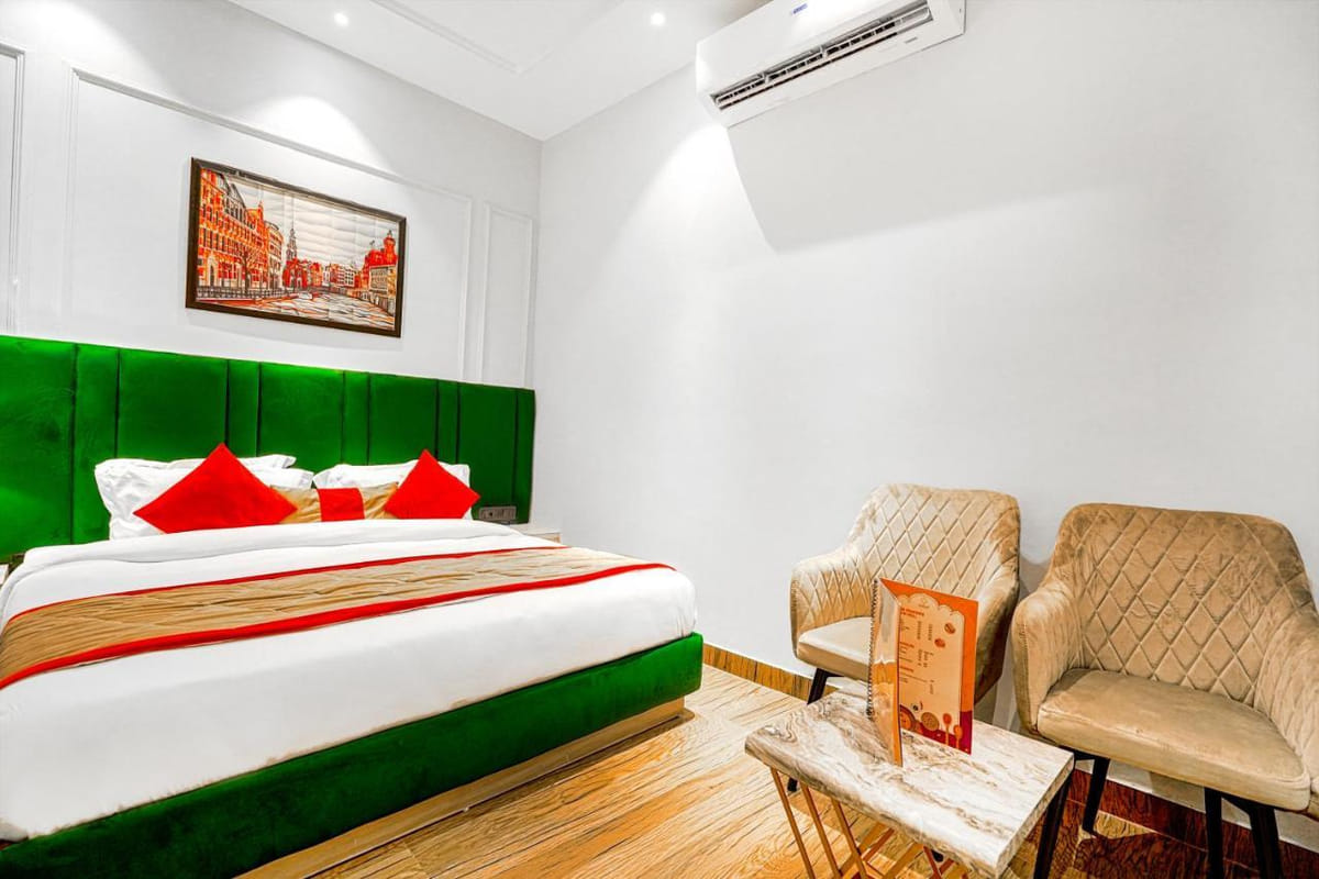 A Deluxe room at Grand Cabbana, with a green padded headboard, red and white bedding, two beige armchairs and framed artwork