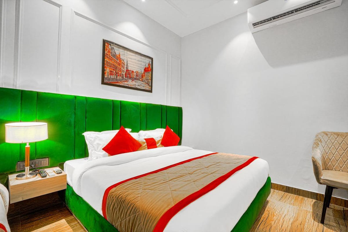 A Deluxe room at Grand Cabbana, with a green padded headboard, a lit bedside lamp, red cushions and an armchair
