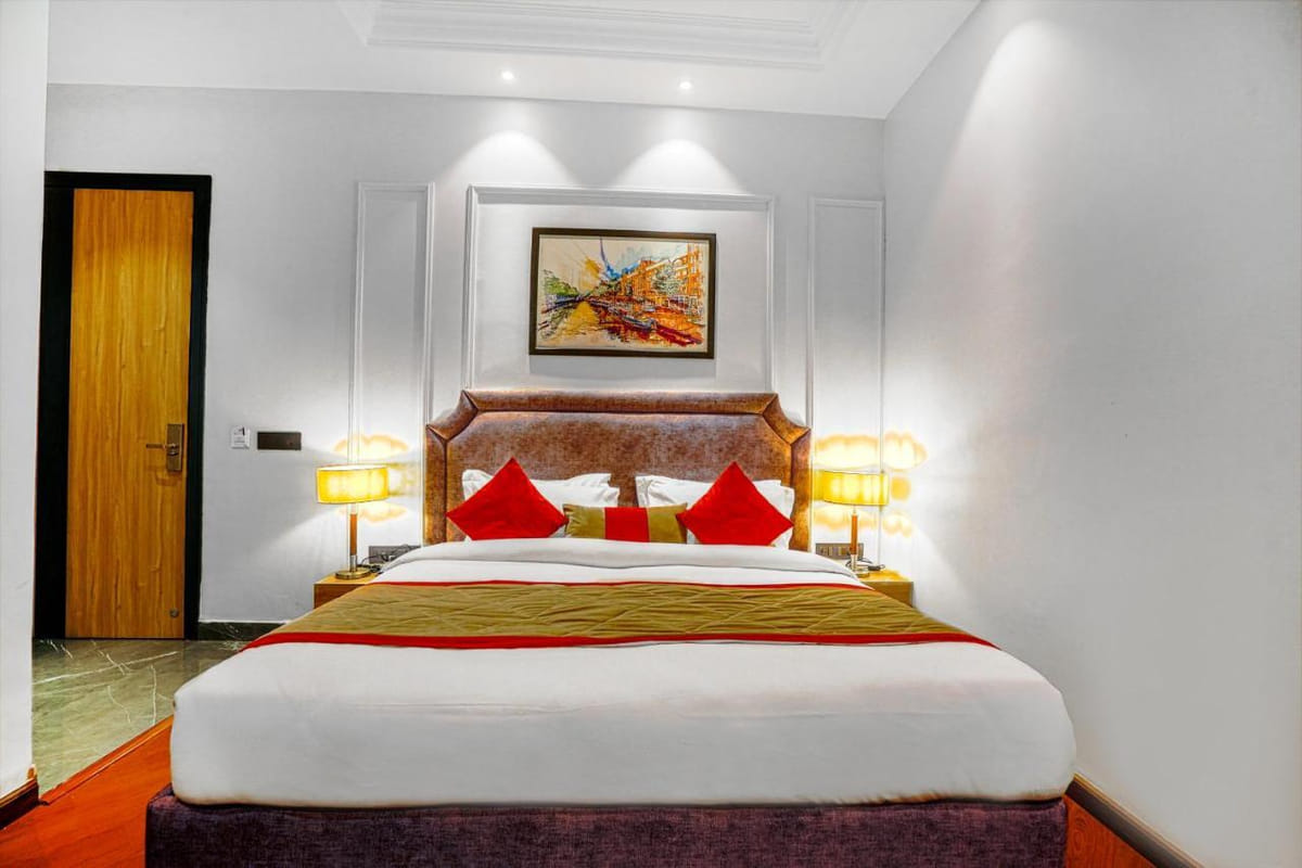 A Super Deluxe room at Grand Cabbana, with a padded headboard, red cushions, a lamp on either side of the bed