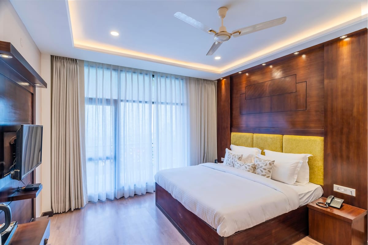 A Deluxe room with valley view at Hotel Karnika, with a yellow padded headboard, timber panelling and sheer curtains