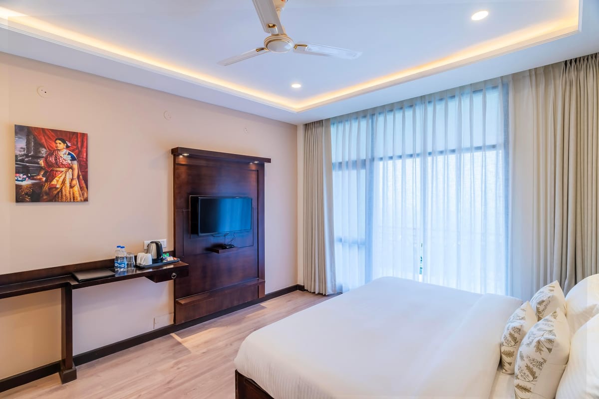 A Deluxe room with valley view at Hotel Karnika, with a long desk beneath the television and framed artwork on the wall