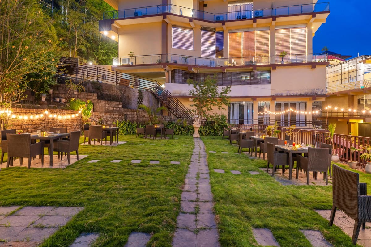 The lawn and terrace at Hotel Karnika at dusk, with outdoor dining tables under strings of lights below the guest balconies