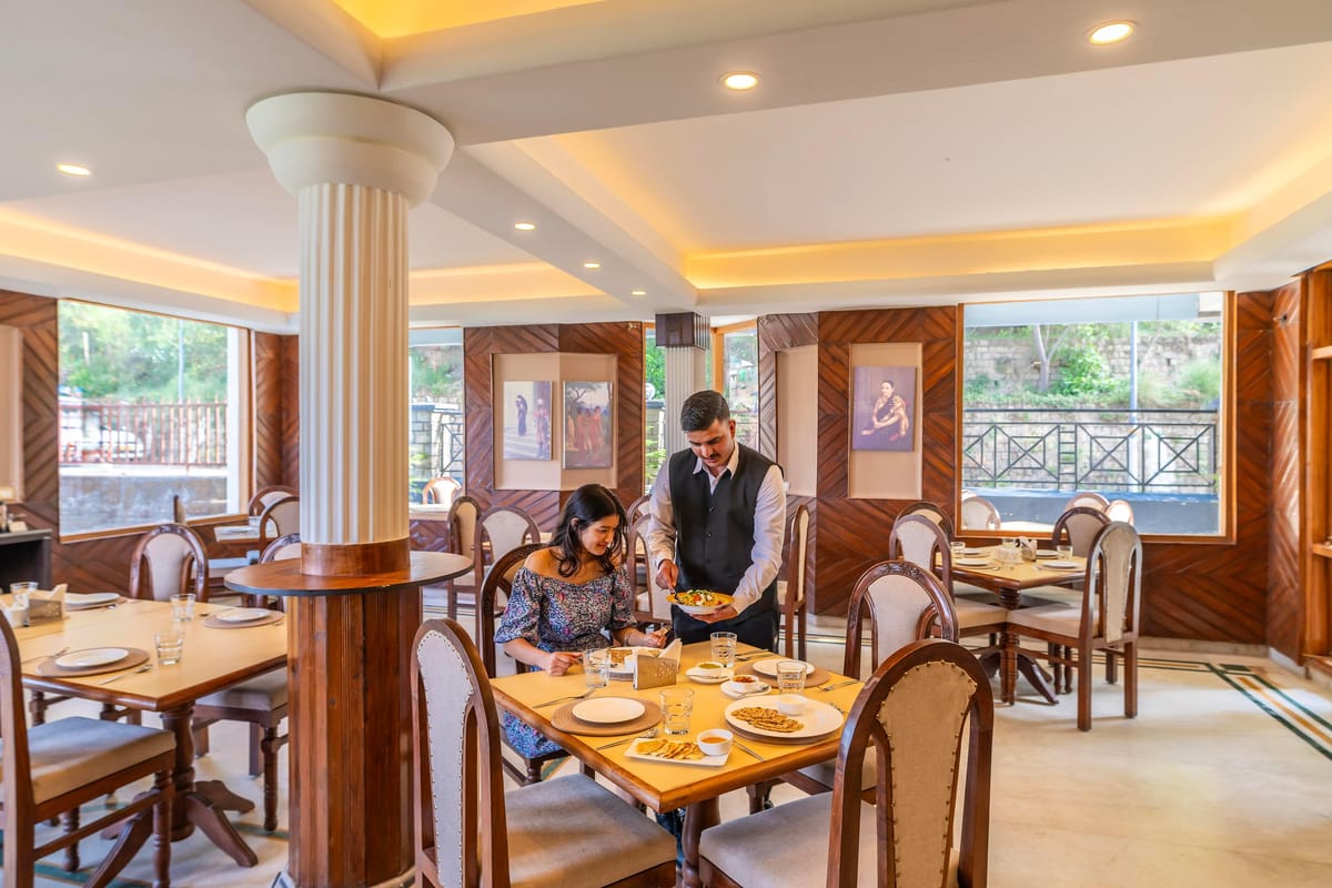 The restaurant at Hotel Karnika, with tables laid around a central column and a waiter serving guests