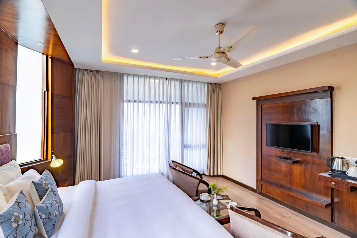 A Super Deluxe room at Hotel Karnika, with a television on the timber panel, a kettle on the counter and curtains