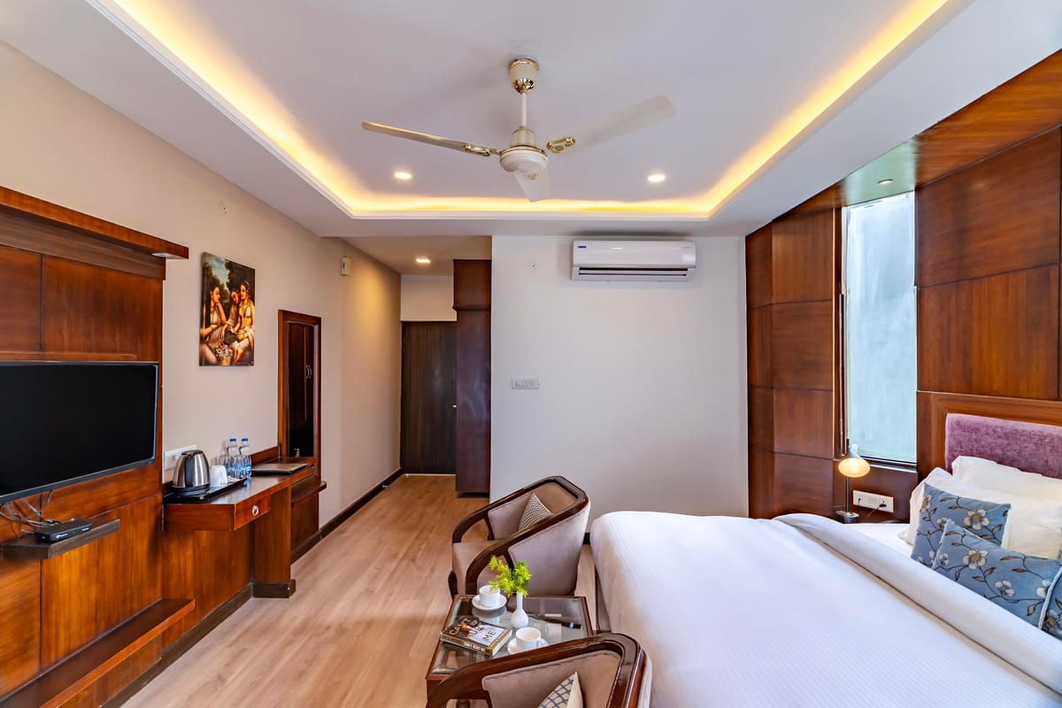 A Super Deluxe room at Hotel Karnika, with a television opposite the bed, a desk set with a kettle