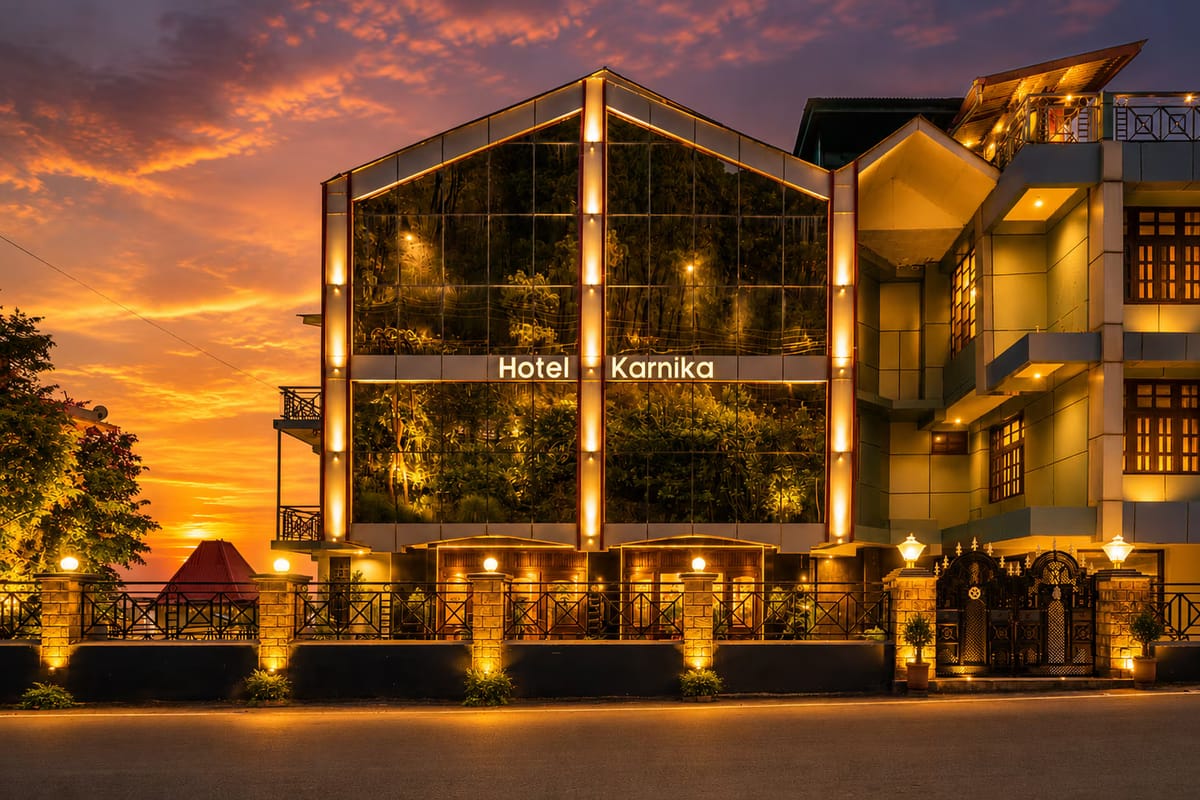 The glass-gabled frontage of Hotel Karnika in Darnu, Dharamshala, lit at sunset with the signage above the entrance canopy