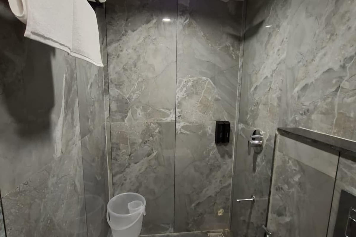 The shower in a guest bathroom at Hotel Shree Radhe By White Panda, behind a glass screen with a hand shower