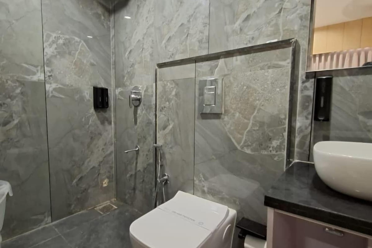 A guest bathroom at Hotel Shree Radhe By White Panda, lined in grey marble-effect tile, with a washbasin, mirror