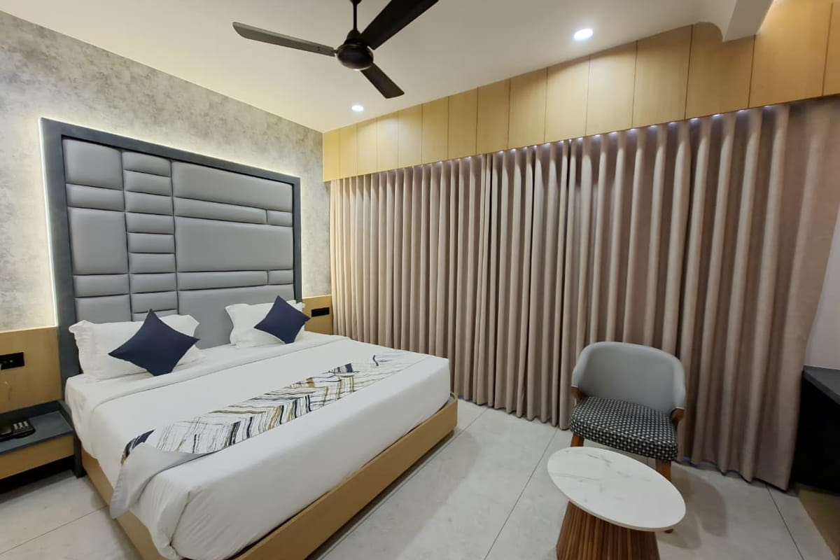 A guest room at Hotel Shree Radhe By White Panda, with a grey padded headboard, blue cushions, full-length curtains