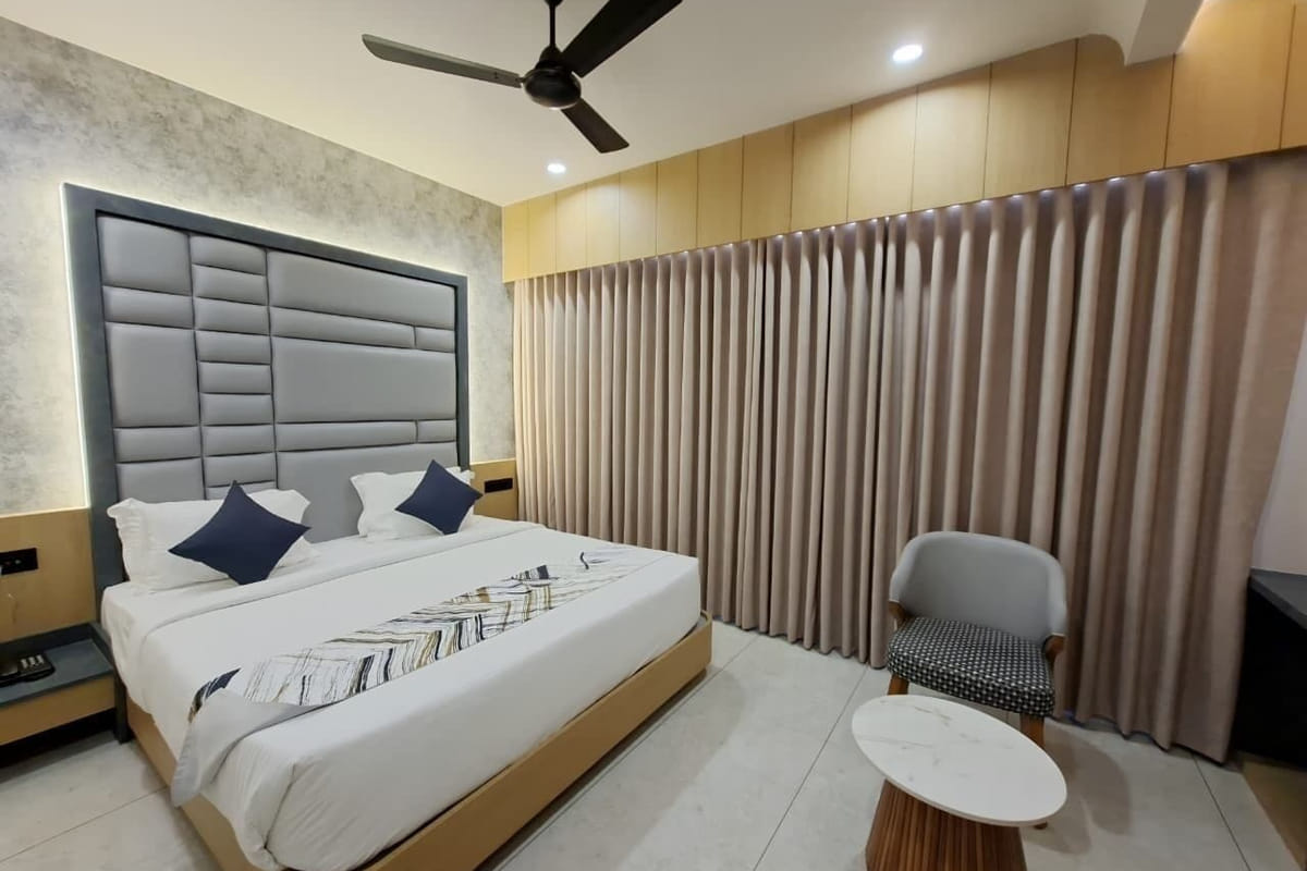 A guest room at Hotel Shree Radhe By White Panda, with a grey padded headboard and blue cushions, a ceiling fan