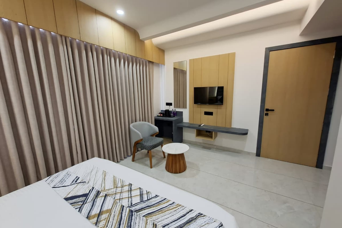 A guest room at Hotel Shree Radhe By White Panda, with curtains drawn along one wall, a television on the timber panel