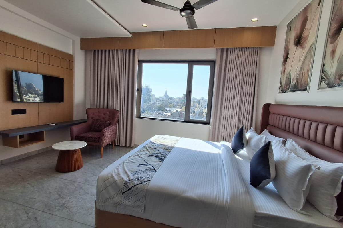 A Temple and Sea View room at Hotel Shree Radhe By White Panda, with a padded headboard, a television opposite and a window