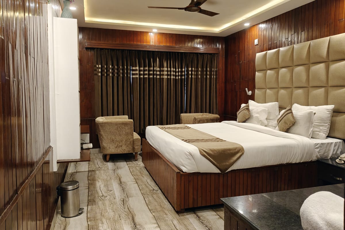 A Queen room at Levelup The Heritage Kud, with dark timber panelling, a padded headboard, armchairs in the corner
