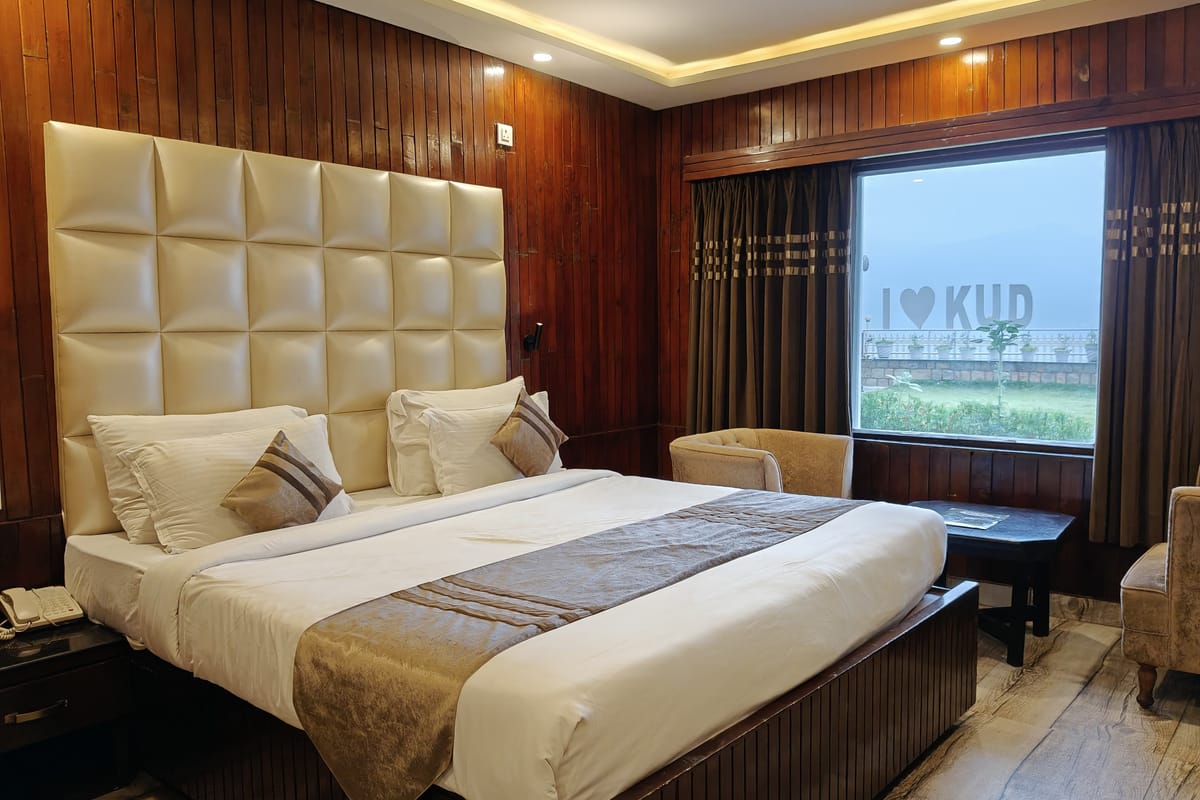 A Queen room at Levelup The Heritage Kud, with a wide white padded headboard, a gold runner across the bed and an armchair