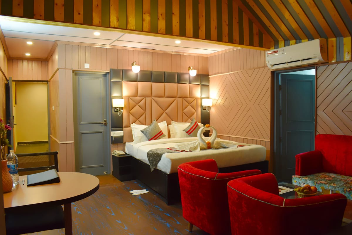 A Family room at Levelup The Heritage Kud, with a padded headboard, two red armchairs drawn up to a table