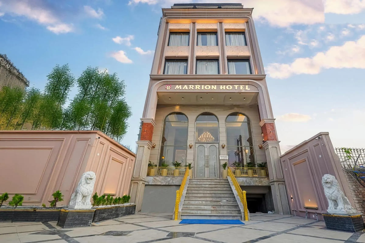 The pale pink facade of Marrion Hotel in Amritsar, with white lion statues either side of the marble steps up to the lit