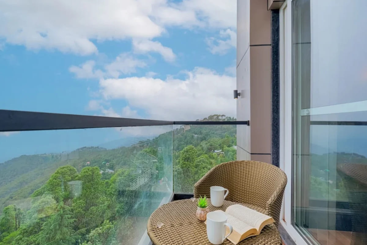 A guest balcony at White Panda Hotel Divine Peaks, with a wicker chair and a small table set with cups, looking out