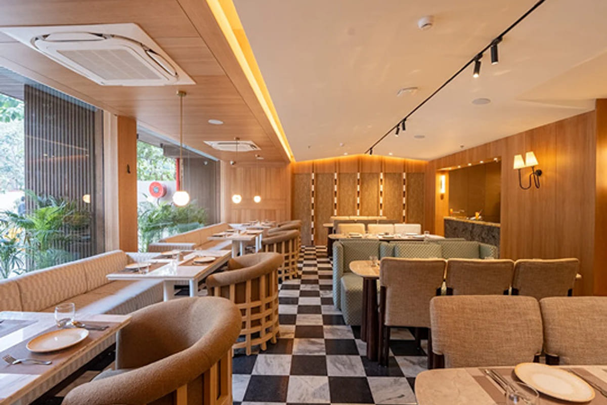 A restaurant interior with banquette seating, a chequerboard floor and warm lighting along a panelled wall