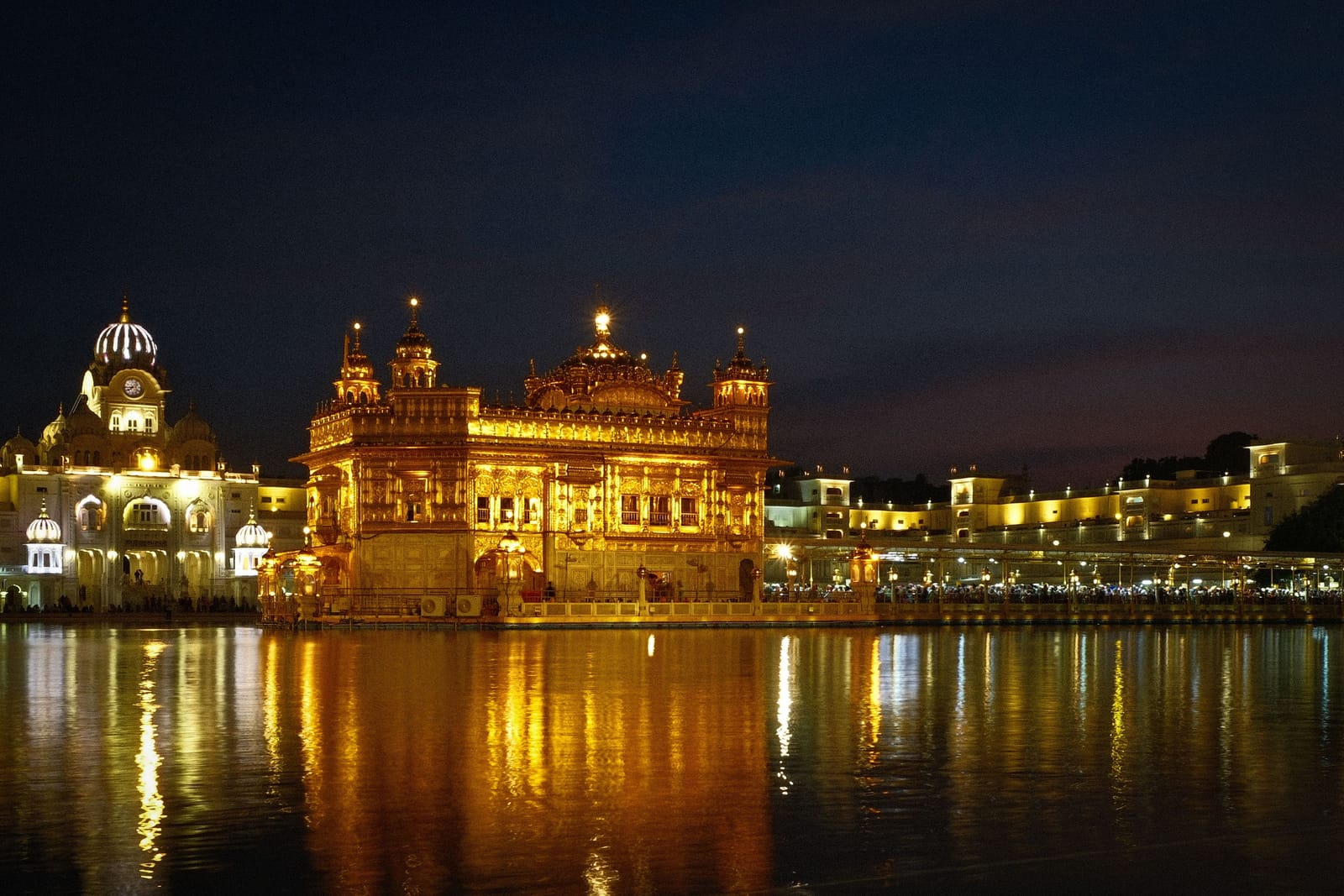 The Golden Temple in Amritsar lit up after dark, the gilded shrine and its reflection stretching across the still tank below