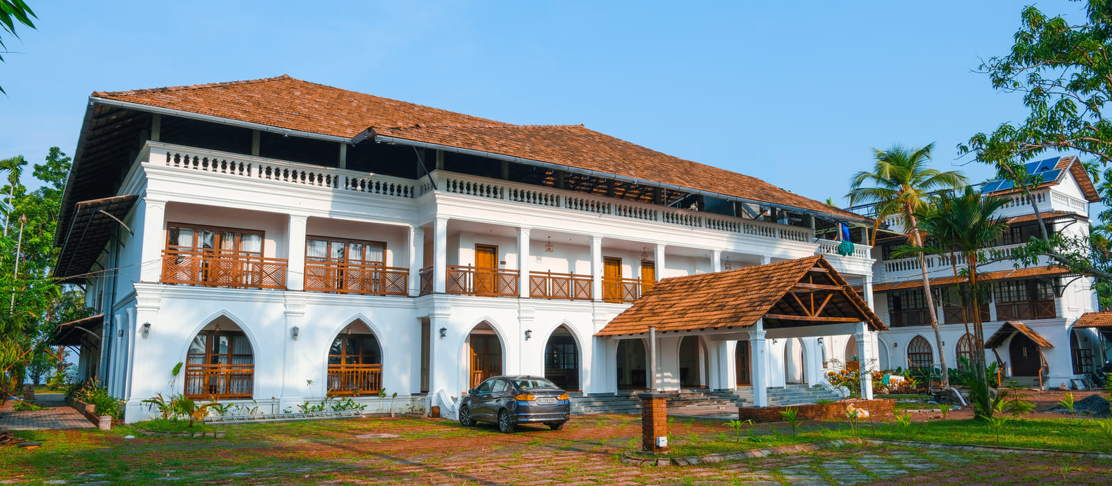 Sanskreti front courtyard with arched Kerala-style verandahs, sloping terracotta-tiled roofs and paved pathway