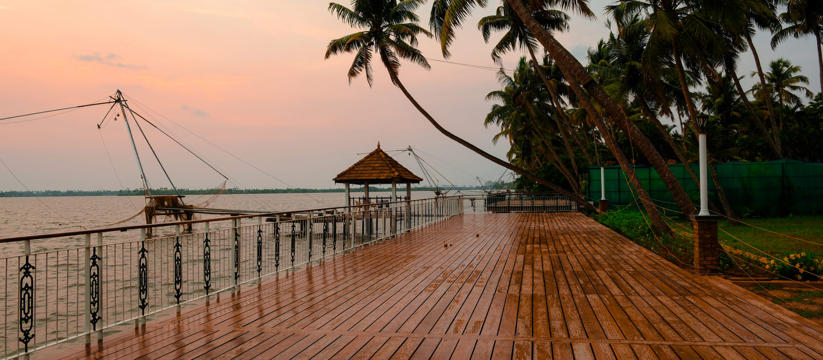Wooden infinity deck and lit gazebo reaching over the Vembanad backwaters at sunset, Sanskreti