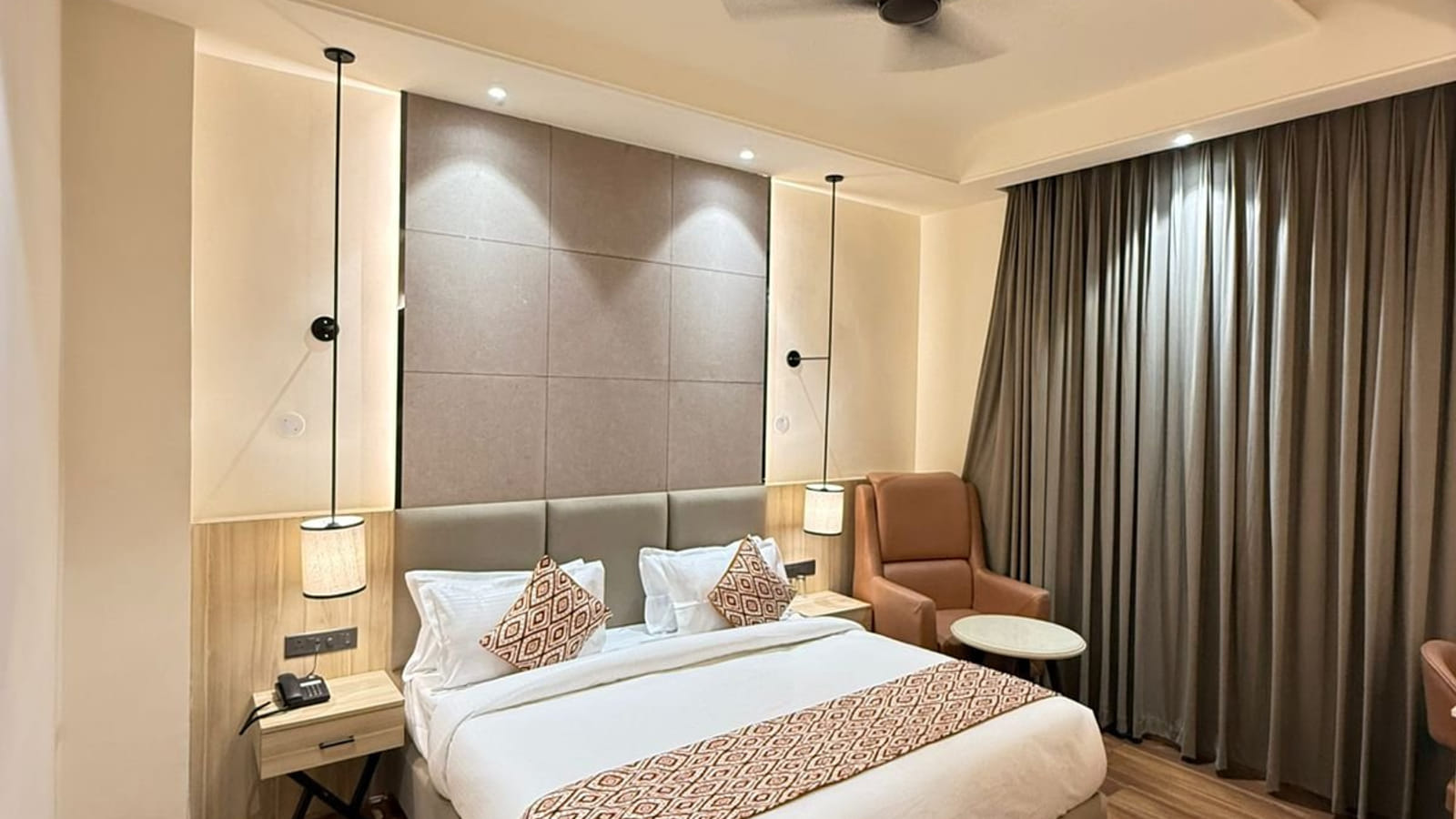 A guest room at Amara Portico, with a padded headboard, dark full-length curtains