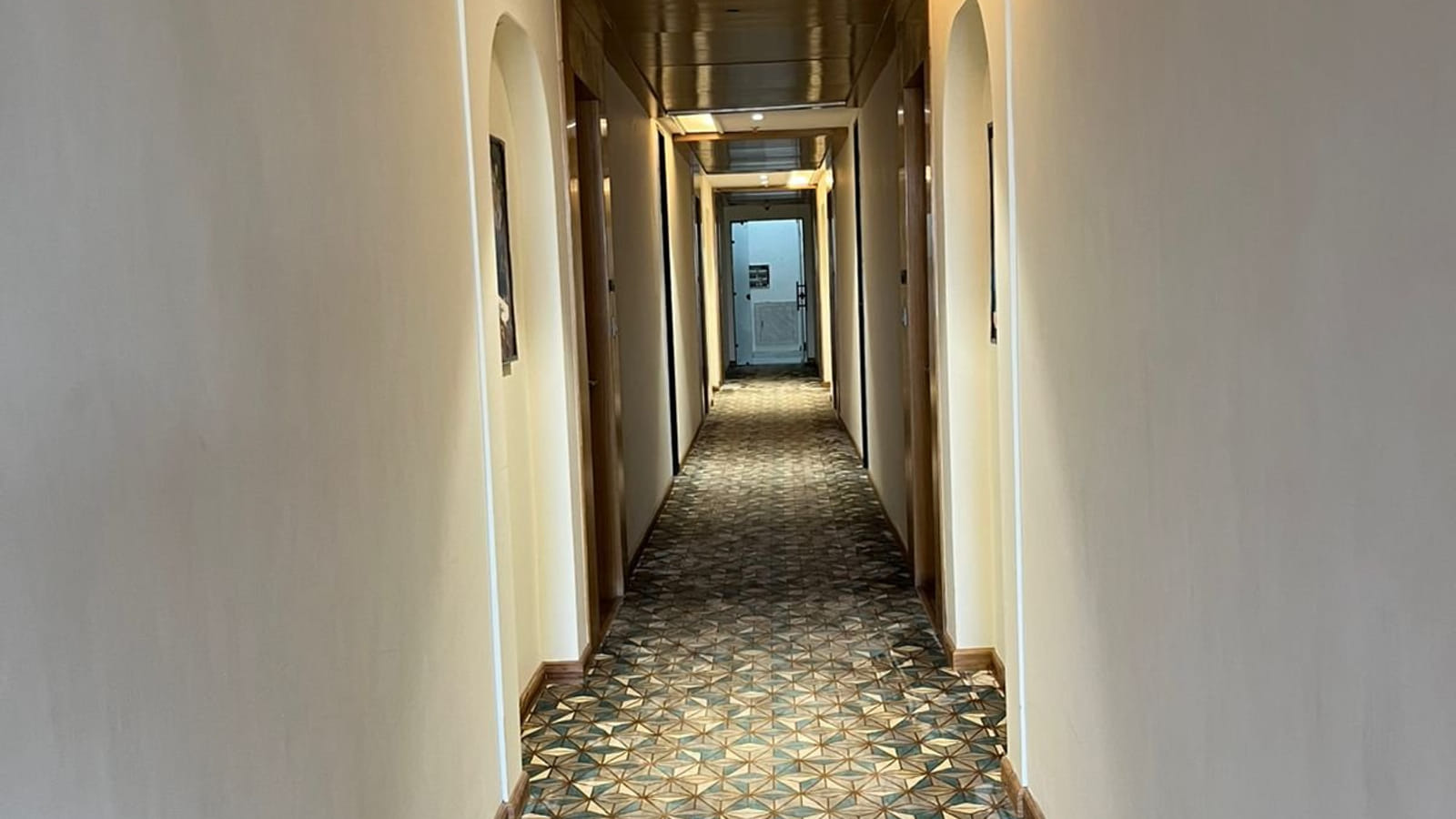 A guest room corridor at Amara Portico, running between the bedroom doors on patterned carpet under warm ceiling lighting