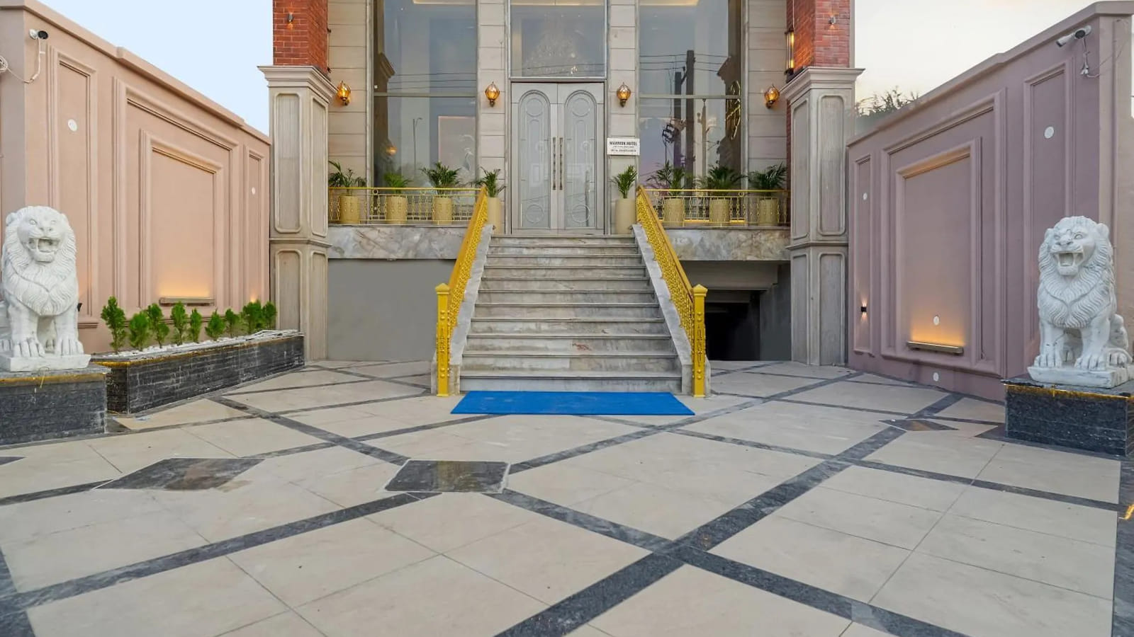 The paved entrance courtyard at Marrion Hotel, Amritsar, with gold handrails on the steps up to the glass doors