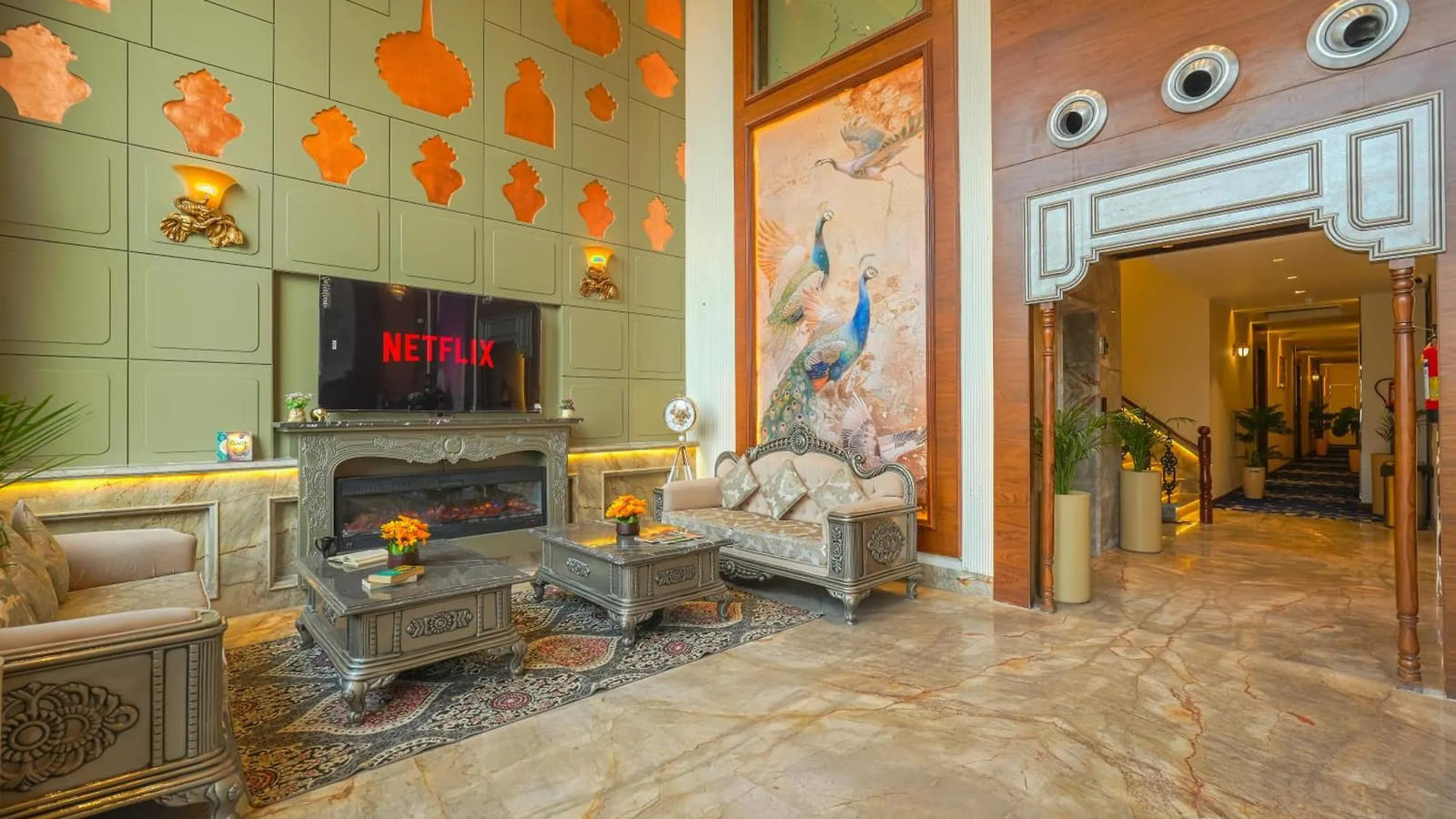 The lobby lounge at Marrion Hotel, with a fireplace below a wall-mounted television, carved silver sofas