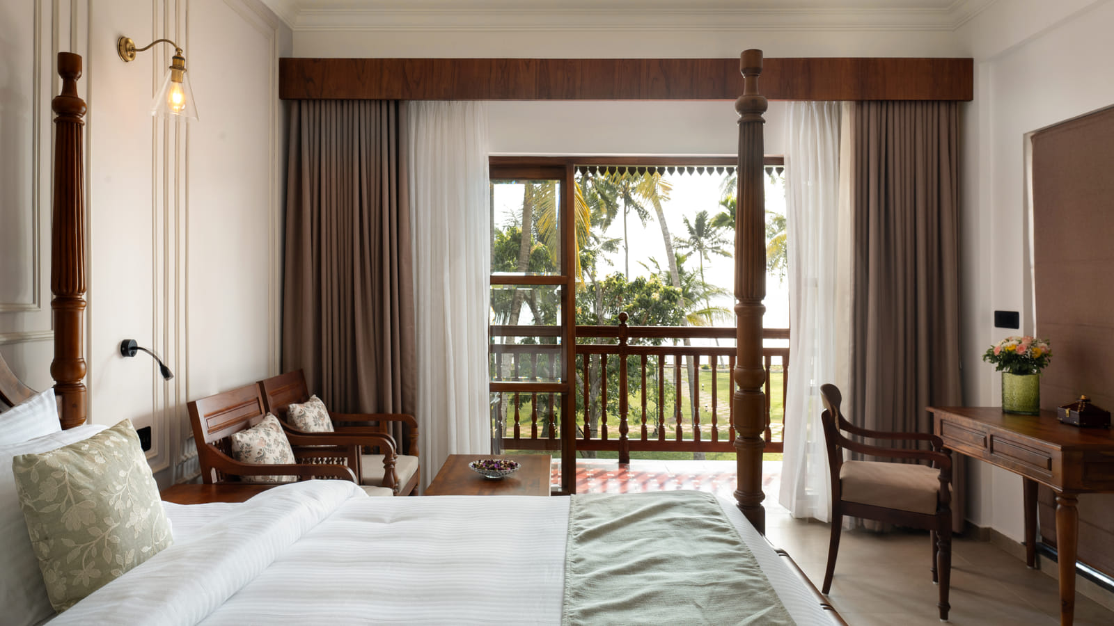 Lake View Room balcony corner with a writing desk, cushioned chair and open doors onto palms and the lake, Sanskreti