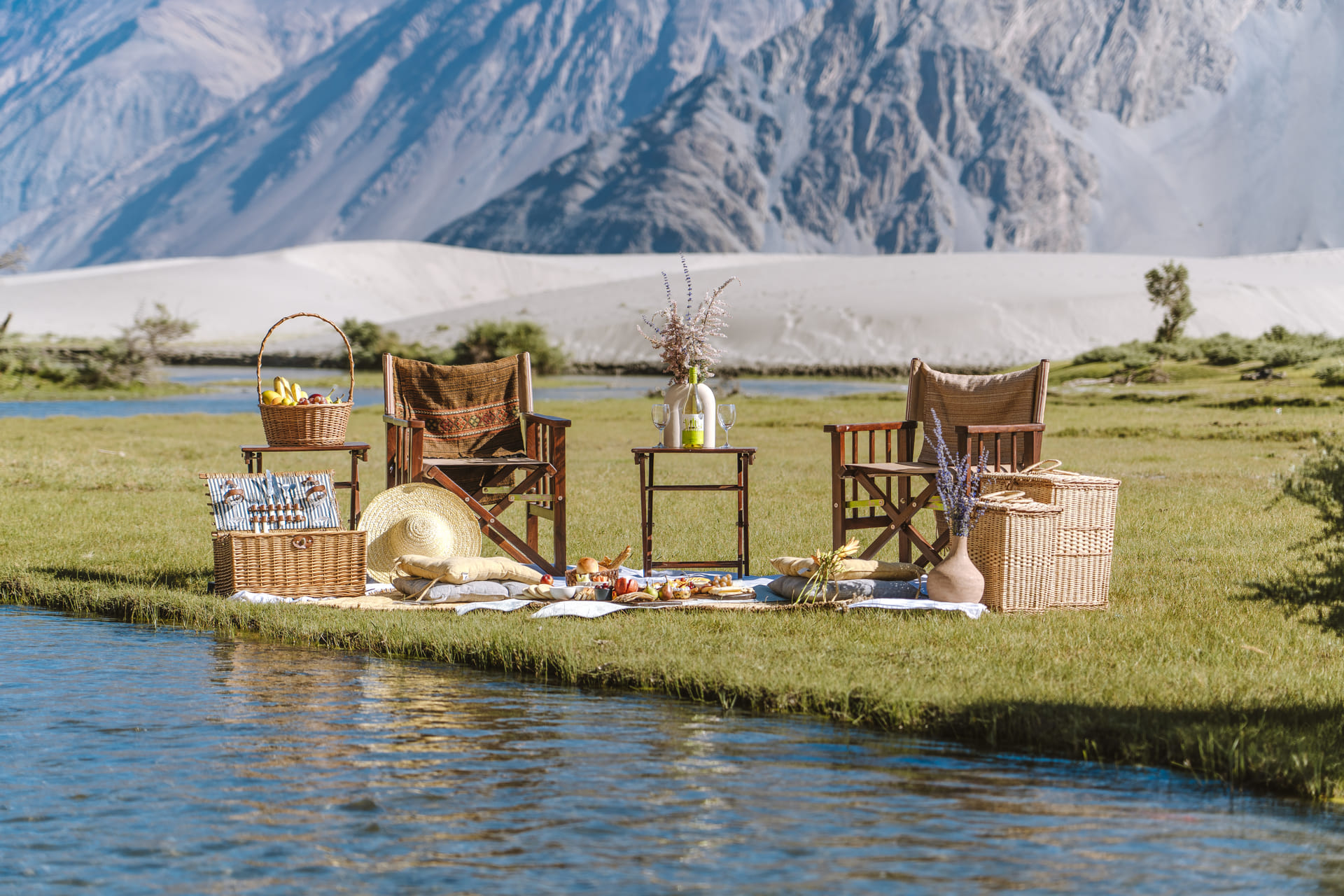 A picnic setup with baskets and chairs beside a river in Nubra Valley