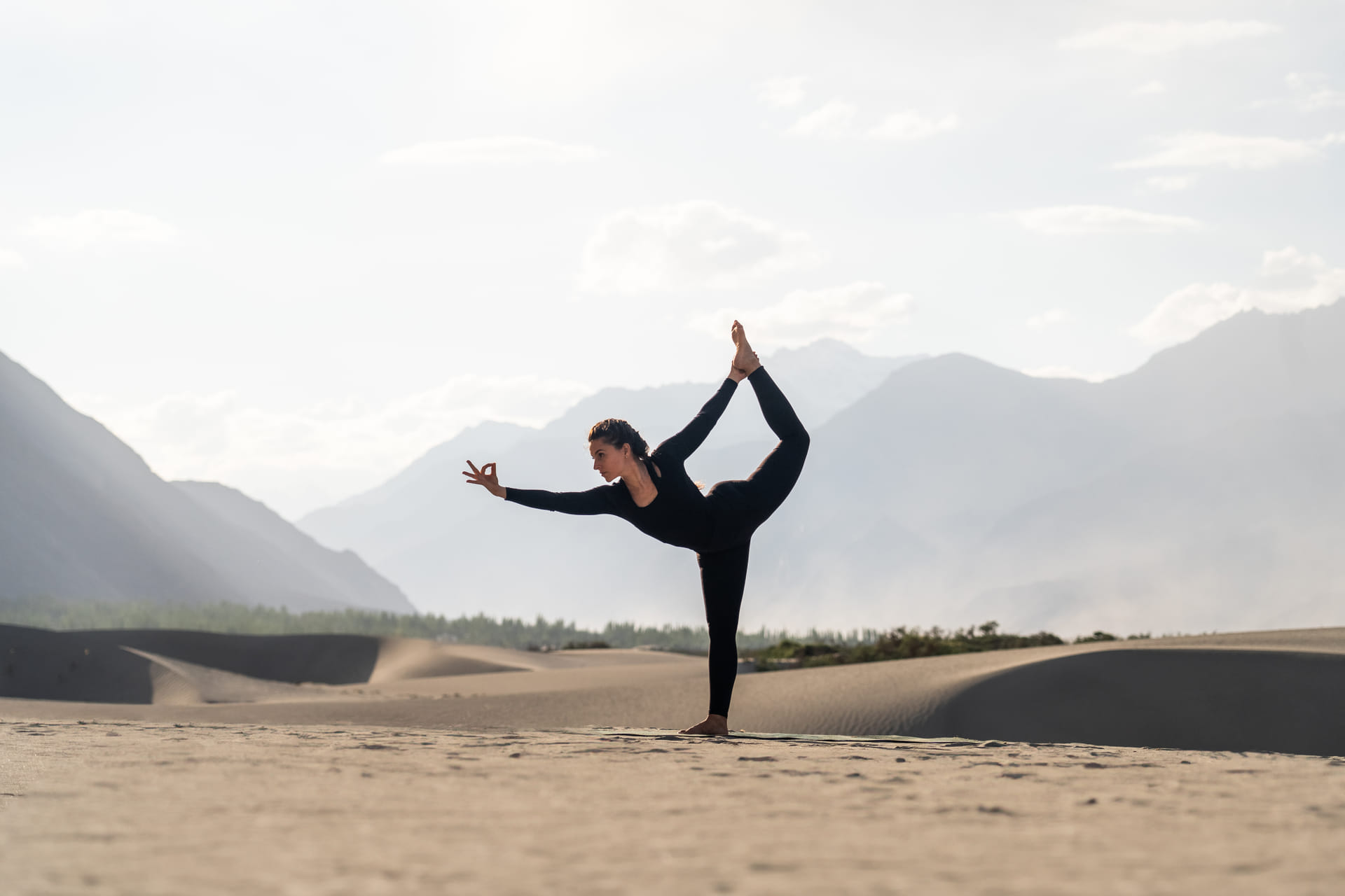 A woman practising yoga on the sand dunes against the Nubra mountains at sunrise