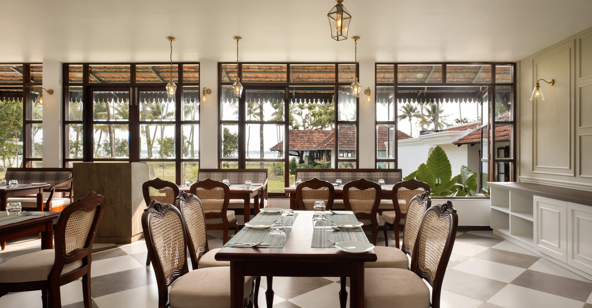 The Lilly's restaurant with cane sofa dining chairs, low wooden tables and tall windows opening to palms and the lake, Sanskreti, Kumbalanghi