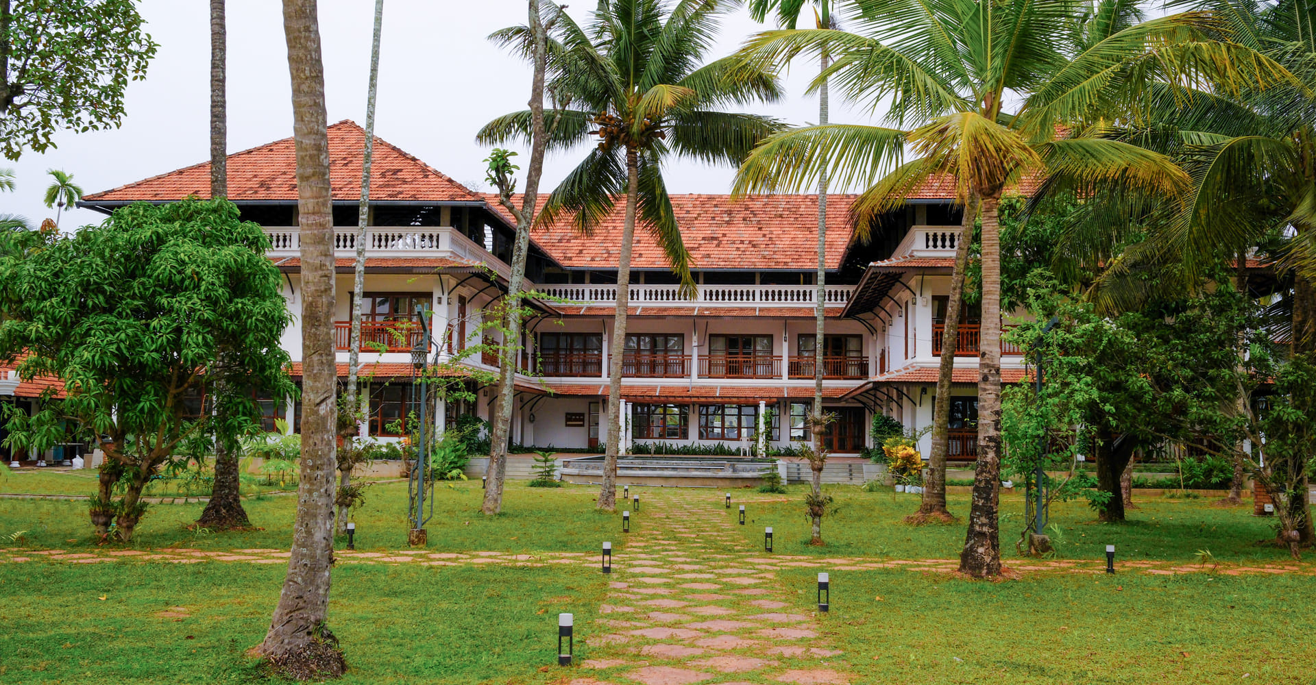 Sanskreti resort exterior with white heritage-style façade, red-tiled roof, coconut palms and landscaped garden, Kumbalanghi, Kochi