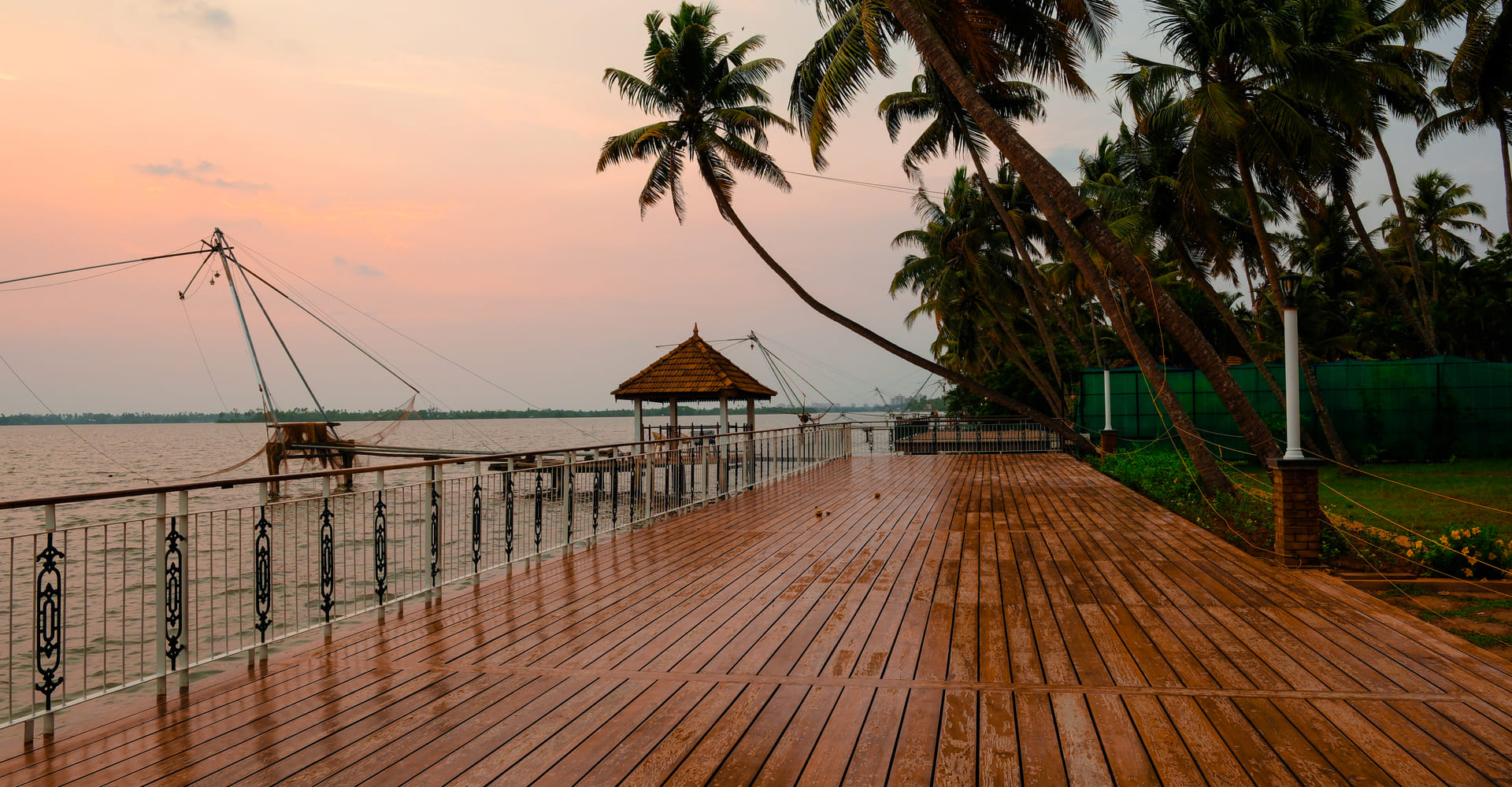 Sanskreti waterfront deck with a wooden gazebo and lounge chairs, sunset over the backwater and palms, Kumbalanghi, Kochi