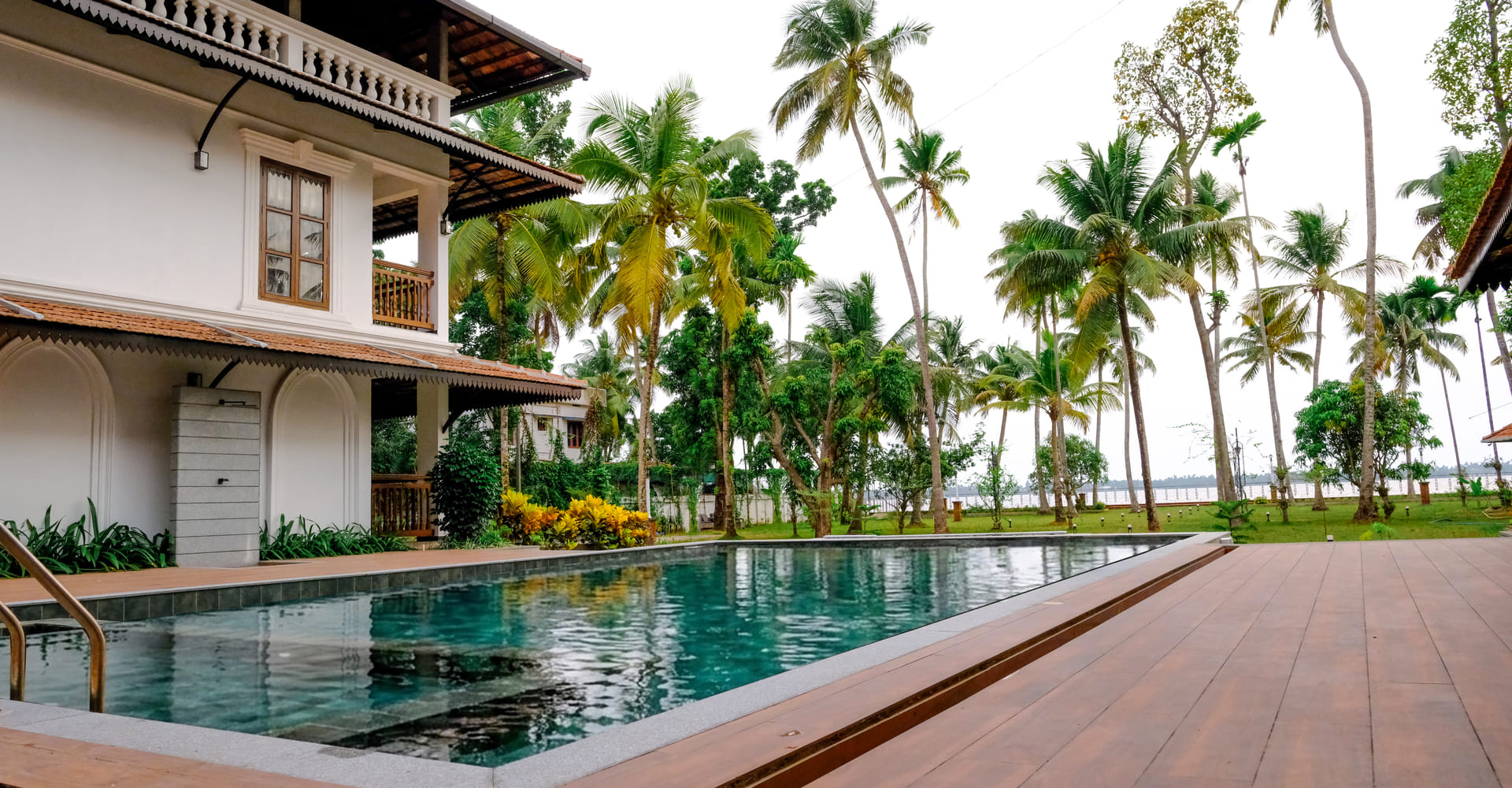 Sanskreti infinity pool blending into the backwater with palm-lined far shore and loungers on the deck, Kumbalanghi, Kochi