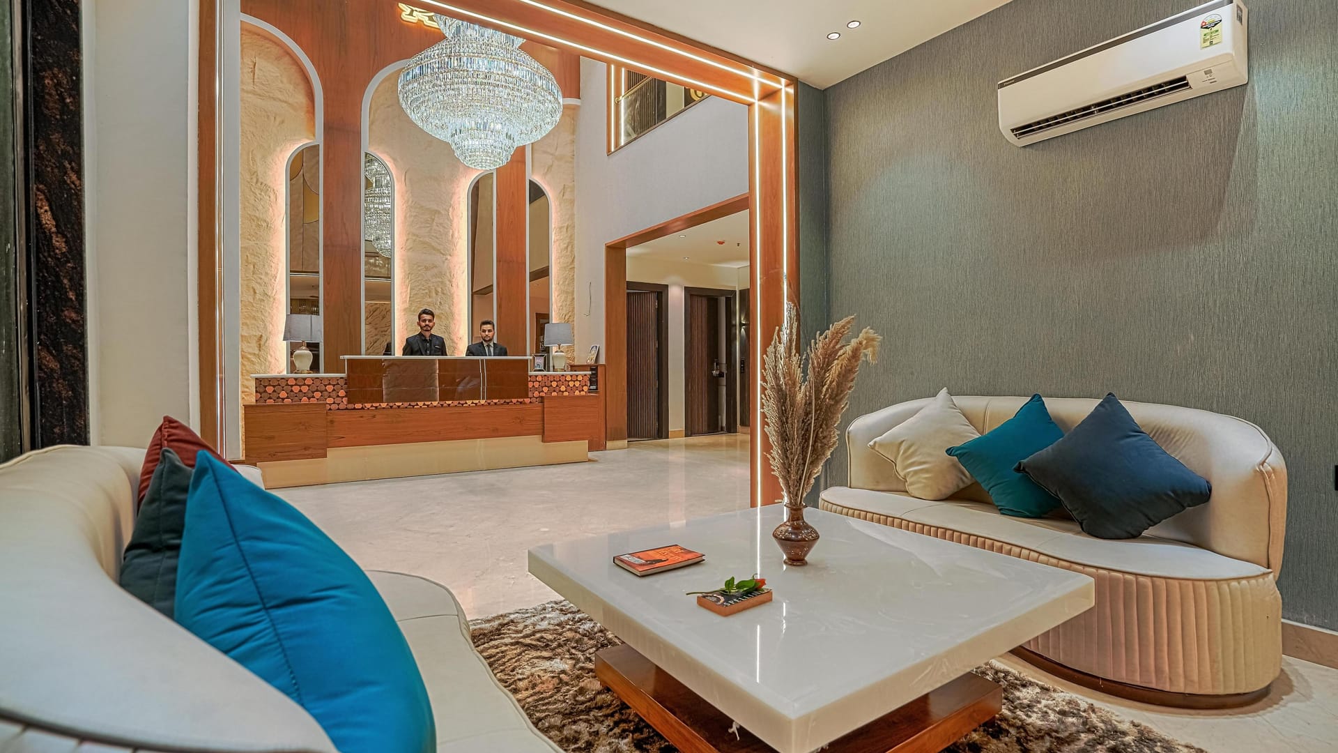 The lounge at Aura Bliss, with curved cream sofas and blue cushions around a low table, a chandelier