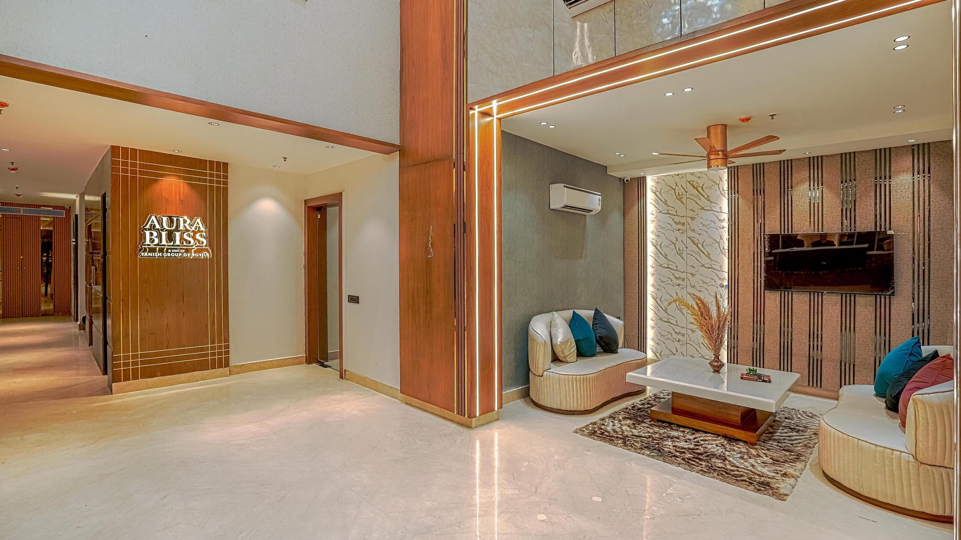 A second lounge area at Aura Bliss, with armchairs around a low table, a television on the fluted timber wall