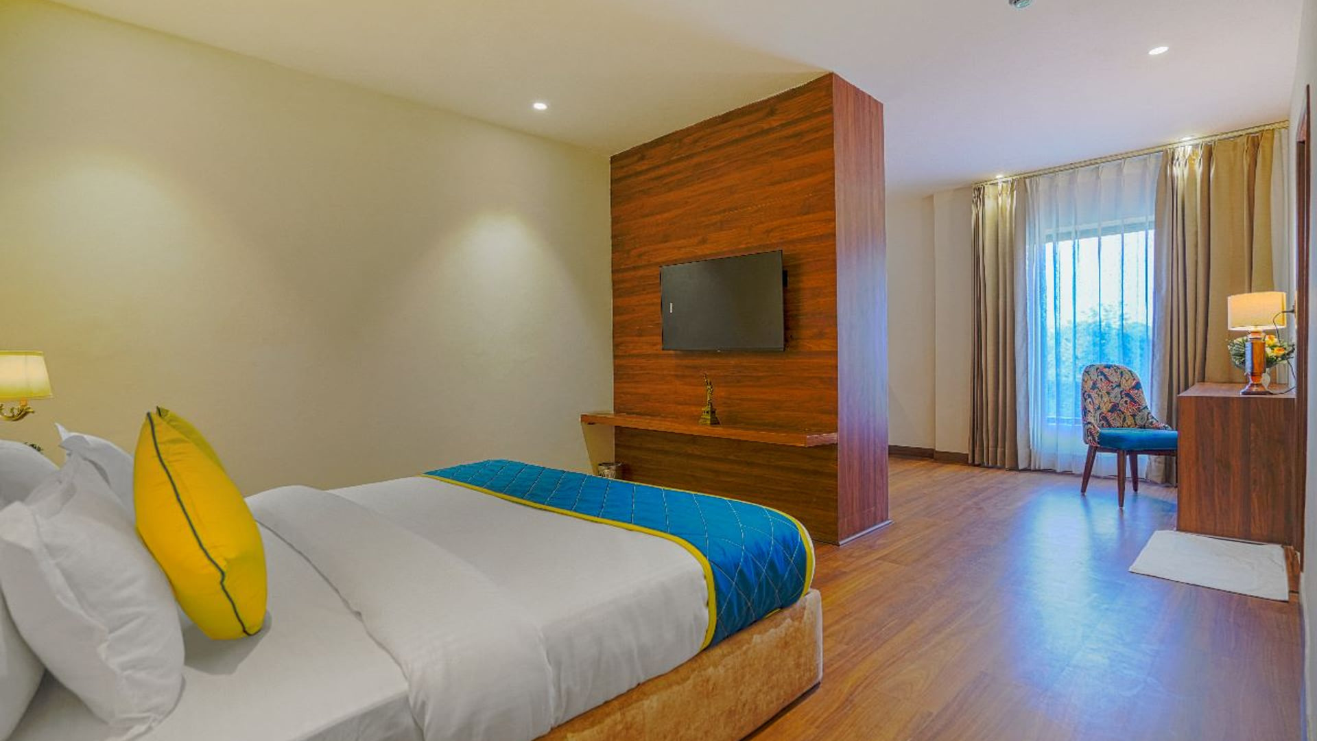 A Suite at Escala Hotel, with a wall-mounted television on a timber panel facing the bed and a curtained window
