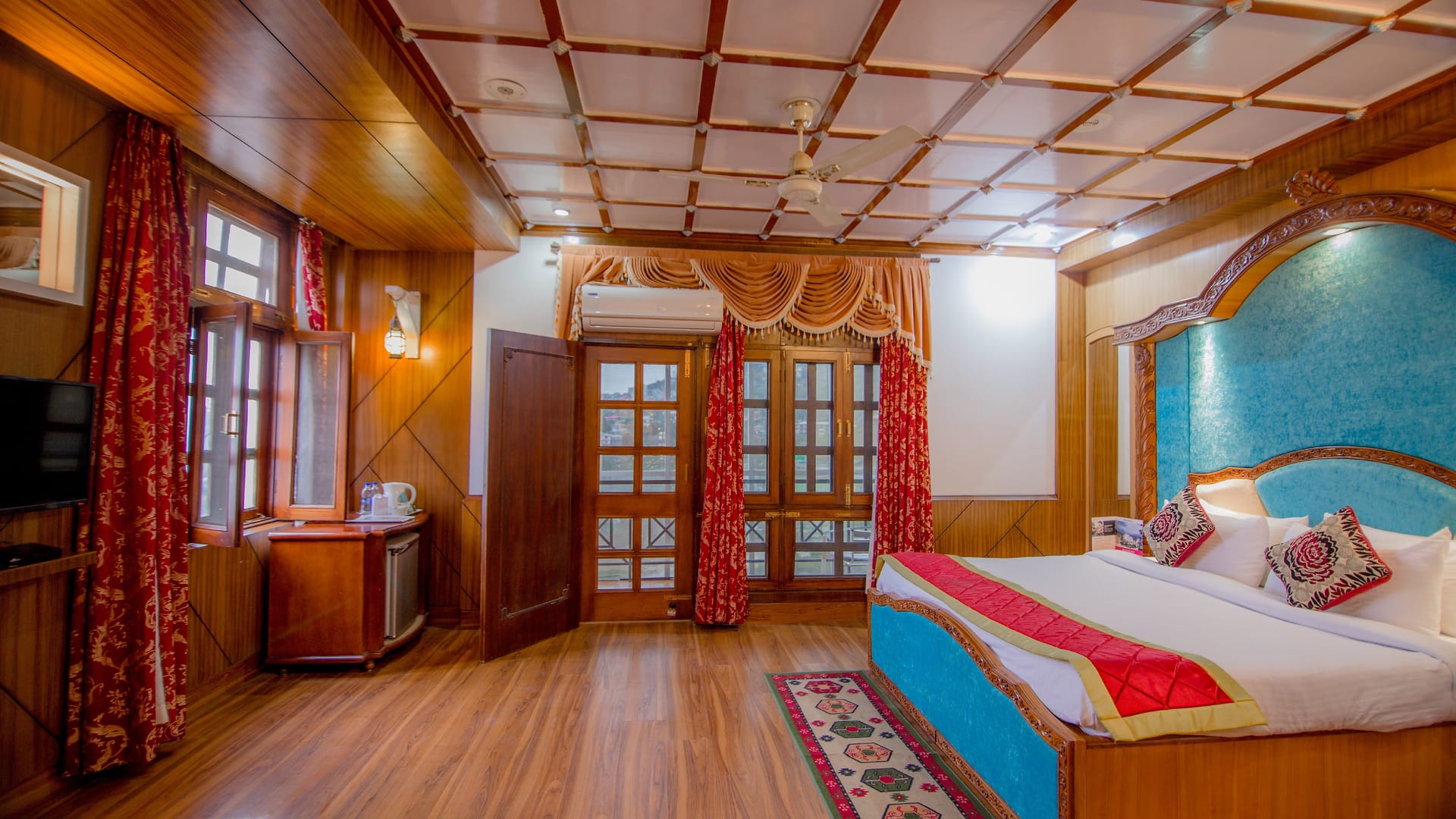 The Maharani Suite at Hotel Karnika, with a coffered timber ceiling, red curtains and a carved bed