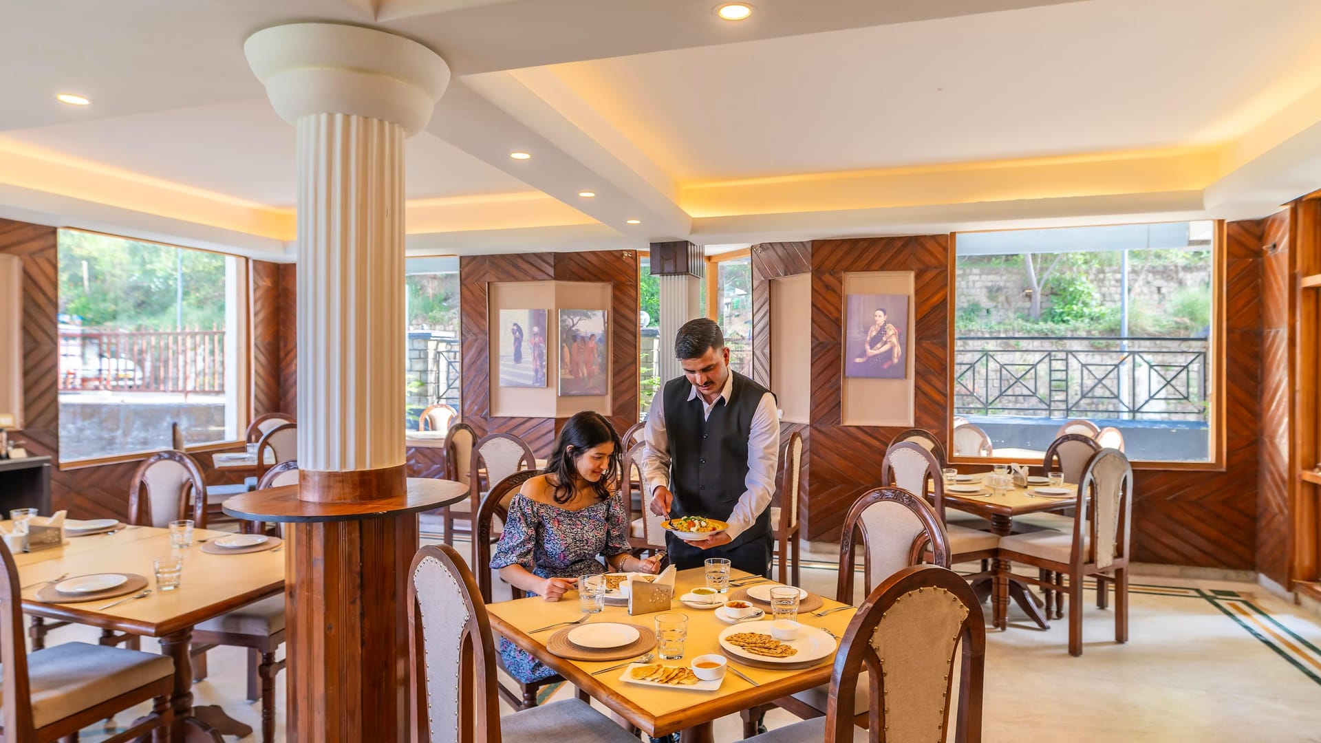 The restaurant at Hotel Karnika, with tables laid around a central column and a waiter serving guests