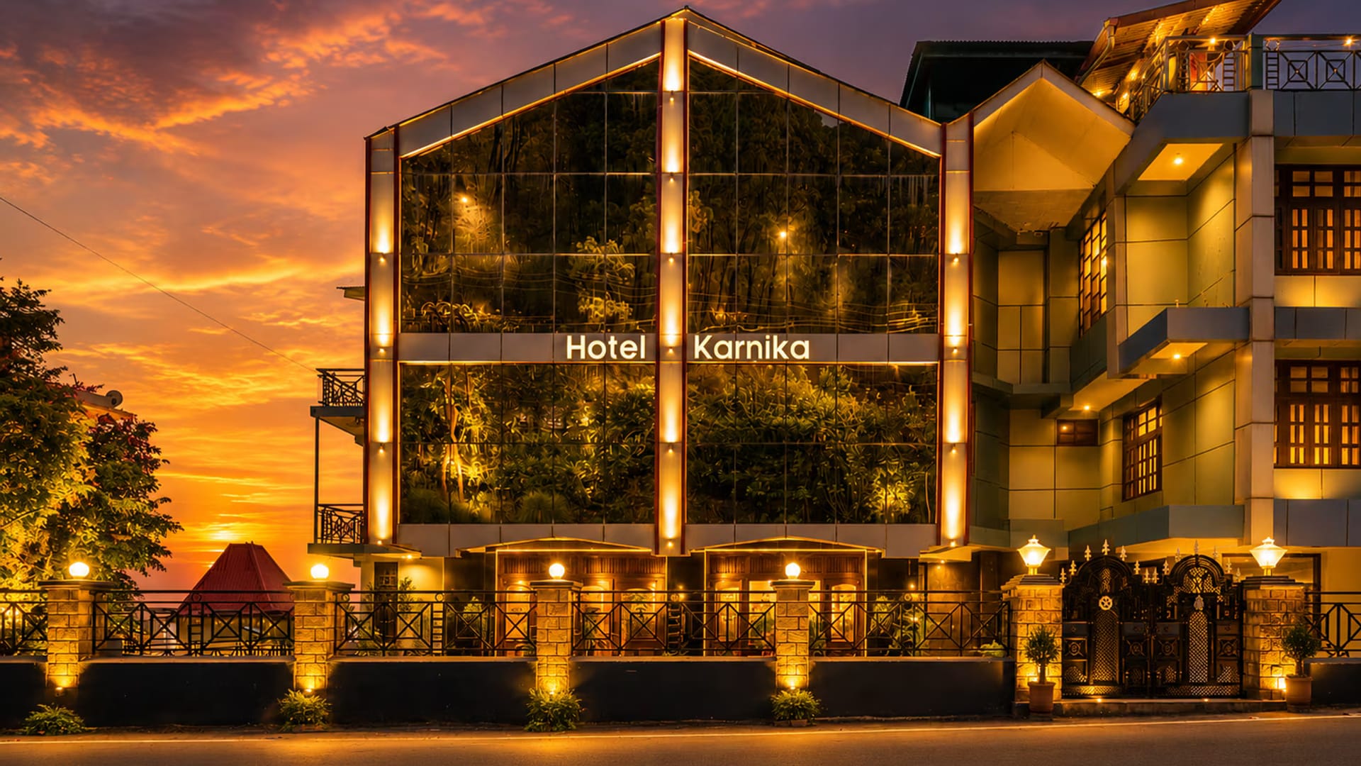 The glass-gabled frontage of Hotel Karnika in Darnu, Dharamshala, lit at sunset with the signage above the entrance canopy