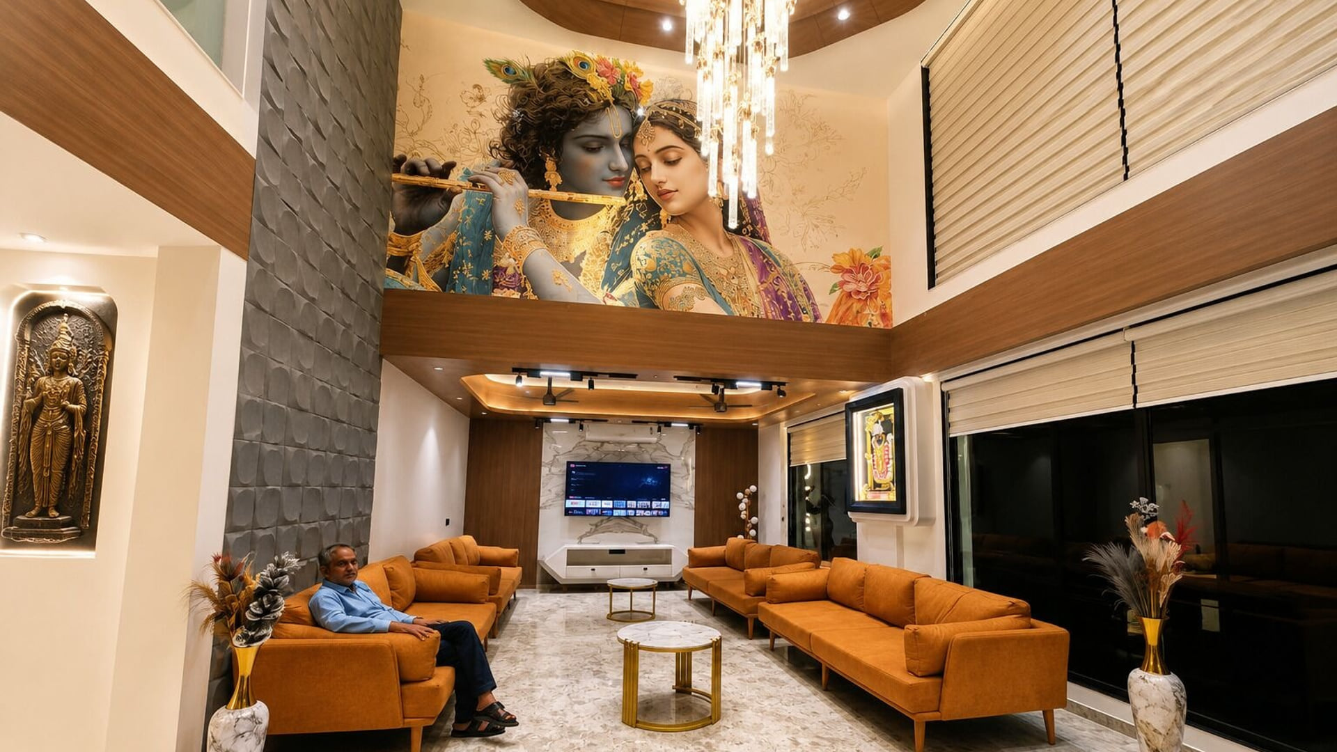 The double-height lobby lounge at Hotel Shree Radhe By White Panda, with a Radha-Krishna mural above the orange sofas