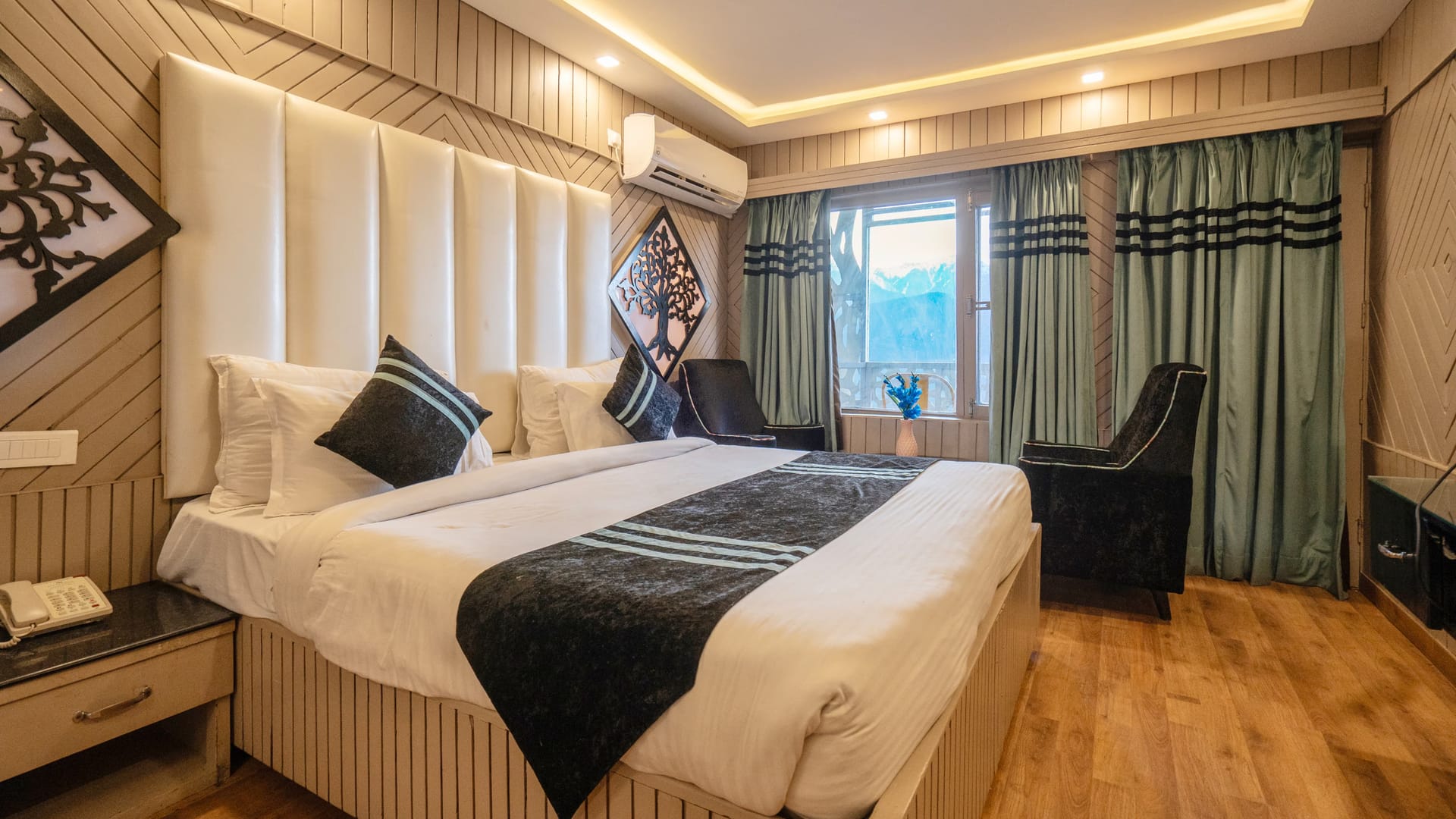 A King room with balcony at Levelup The Heritage Kud, with a tall padded headboard, timber panelling and armchairs