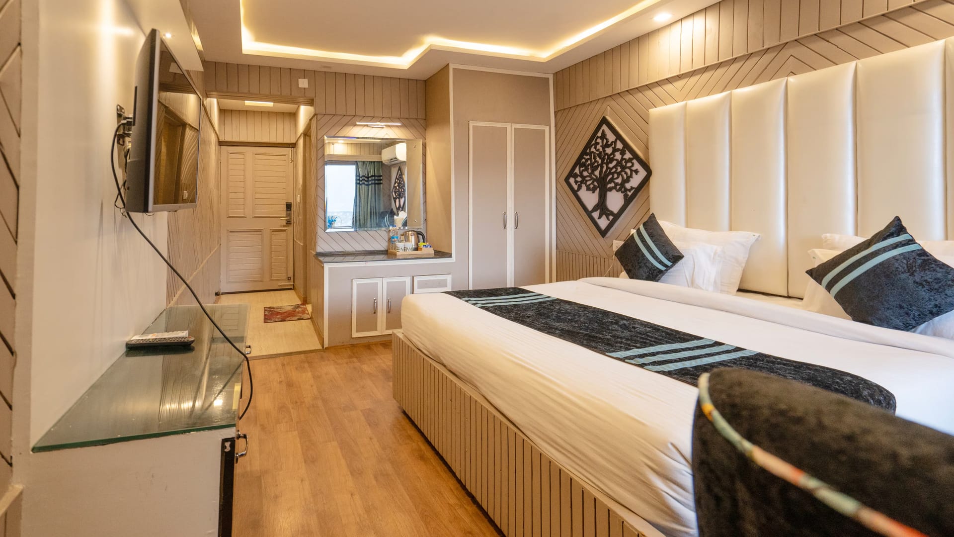 A King room with balcony at Levelup The Heritage Kud, with padded headboard panels, a wall-mounted television