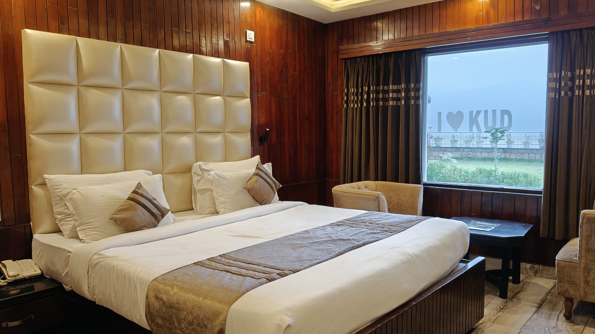 A Queen room at Levelup The Heritage Kud, with a wide white padded headboard, a gold runner across the bed and an armchair