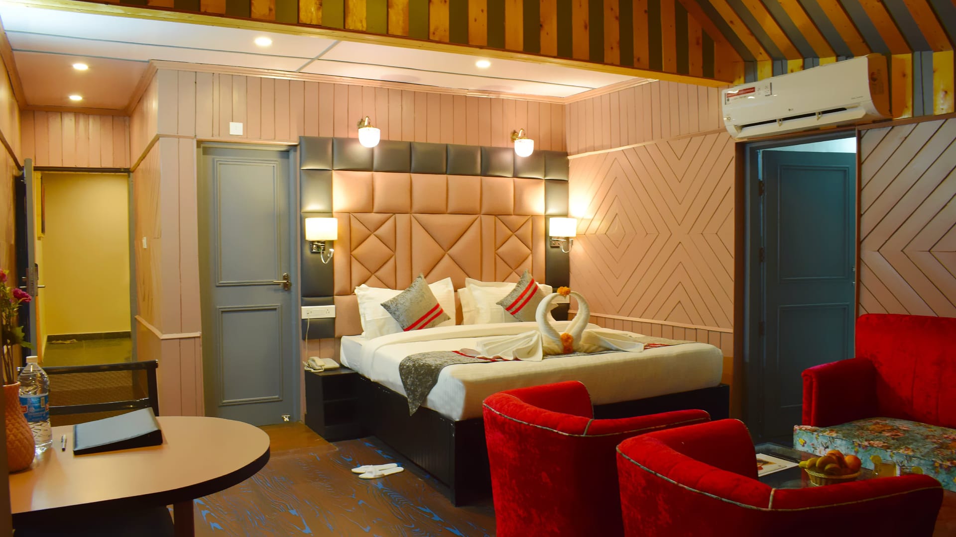 A Family room at Levelup The Heritage Kud, with a padded headboard, two red armchairs drawn up to a table