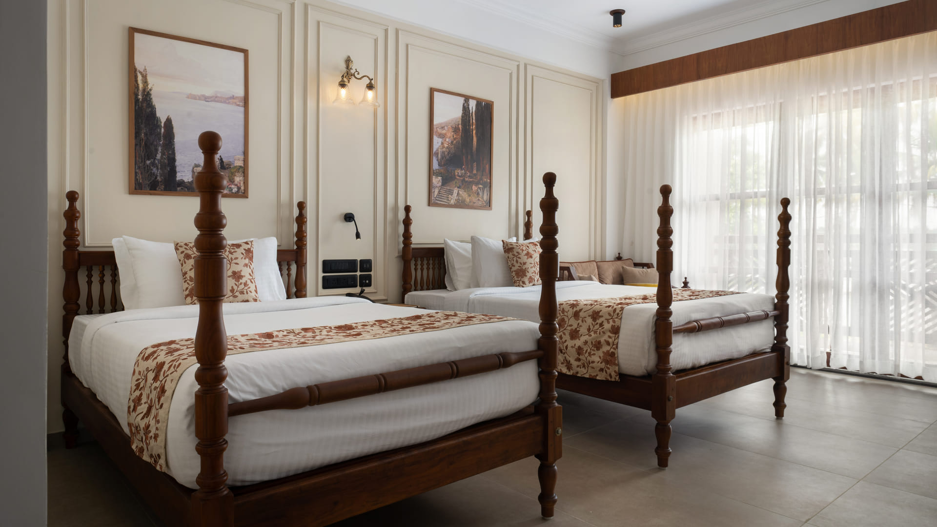 Garden View Room with two four-poster twin beds and pillow shams beneath a wide landscape wall painting, Sanskreti