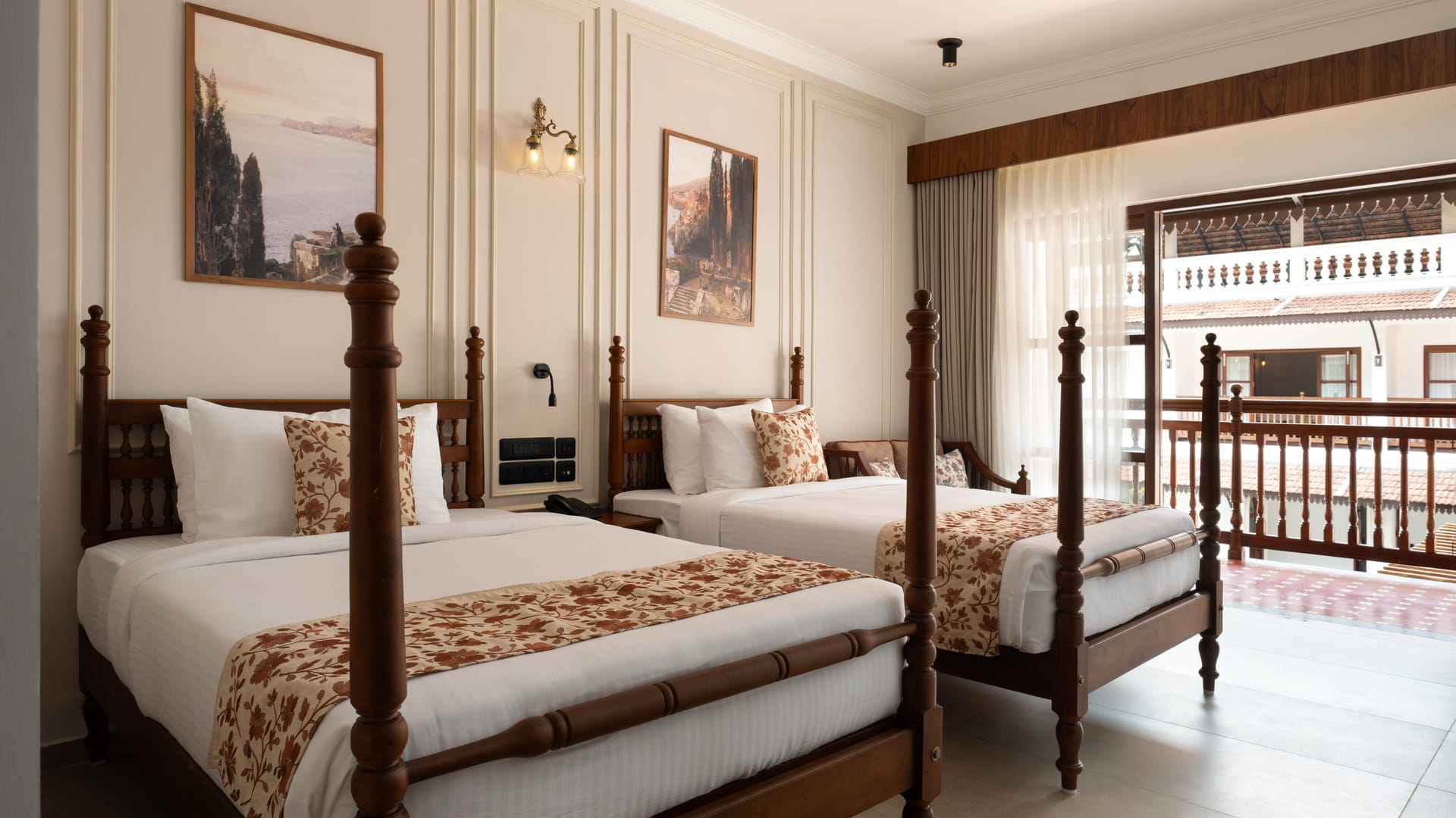 Pool View Twin Room with two four-poster twin beds, cane headboards and pink floral runners, pool-side balcony doors behind, Sanskreti