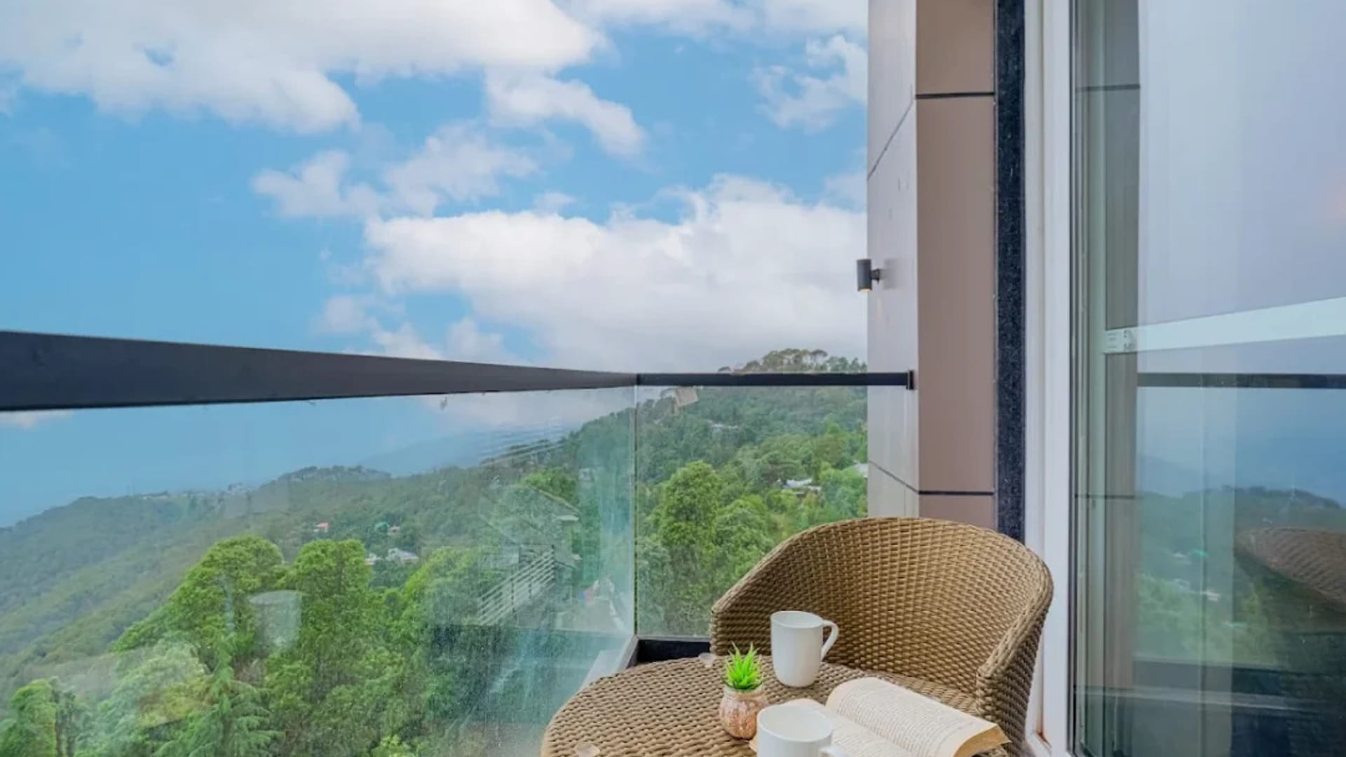 A guest balcony at White Panda Hotel Divine Peaks, with a wicker chair and a small table set with cups, looking out